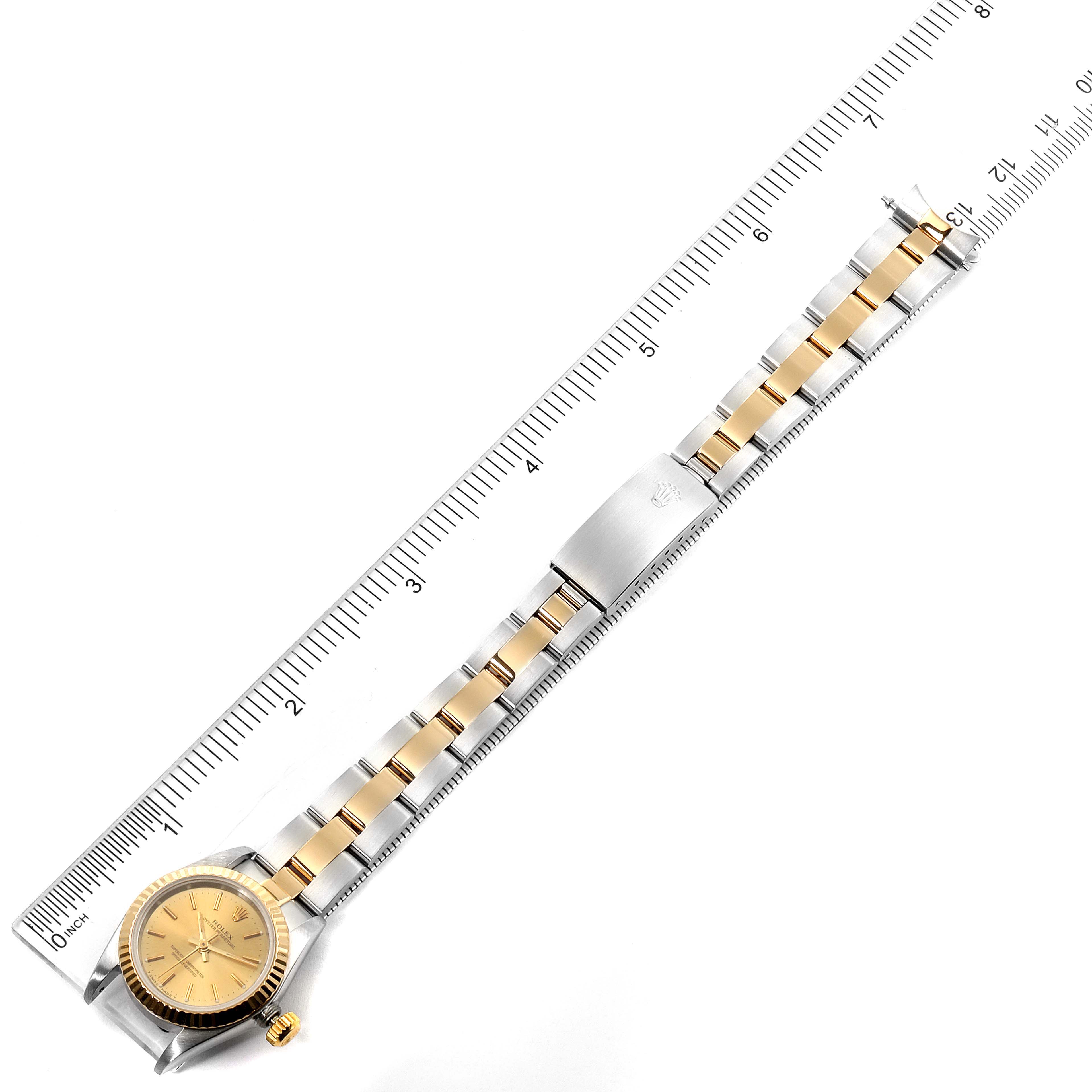 The Rolex Oyster Perpetual 67193 Women's Steel and Gold (two tone) Champagne Dial 67193 Women's Steel and Gold (two tone) Champagne Dial watch is displayed flat with its face, bezel, crown, and bracelet visible against a measuring scale.