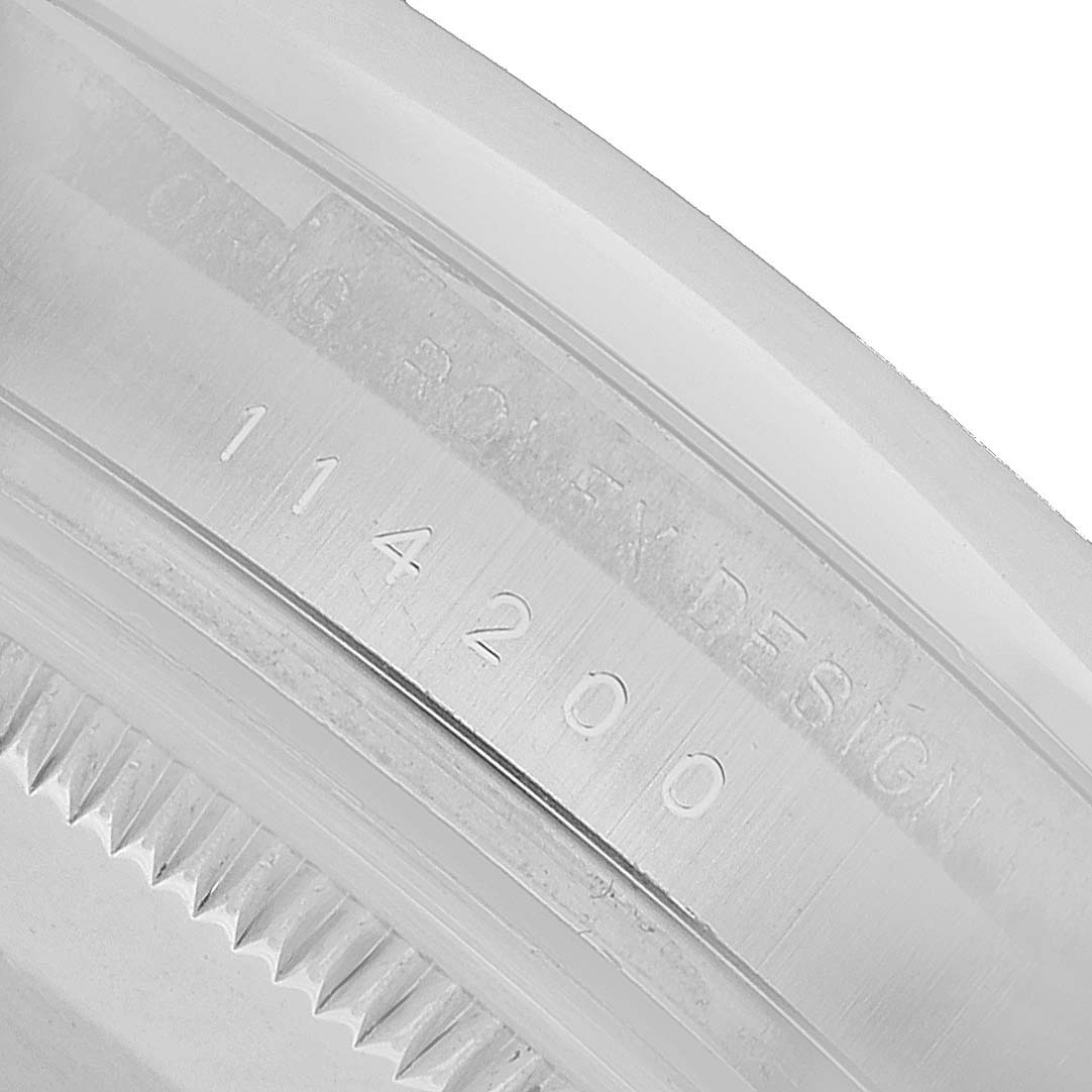 The image shows a close-up of the bezel edge and engraved serial numbers on a Rolex Oyster Perpetual 114200 Men's Stainless Steel Green Dial watch.
