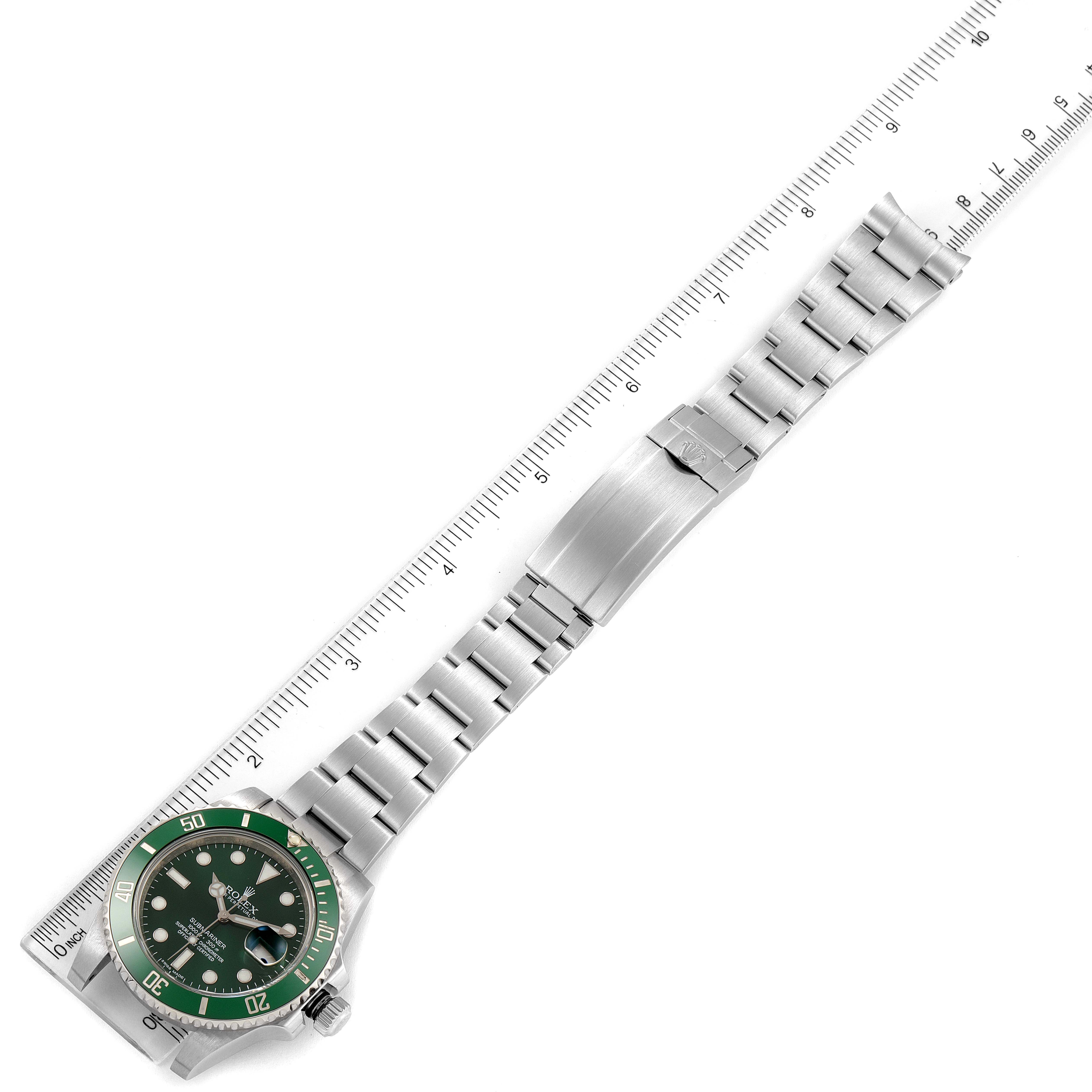 The image shows a top-down view of a Rolex Submariner 116610LV Men
s Stainless Steel Green Dial 116610LV Men
s Stainless Steel Green Dial watch with a green bezel, stainless steel bracelet, and clasp next to a ruler.