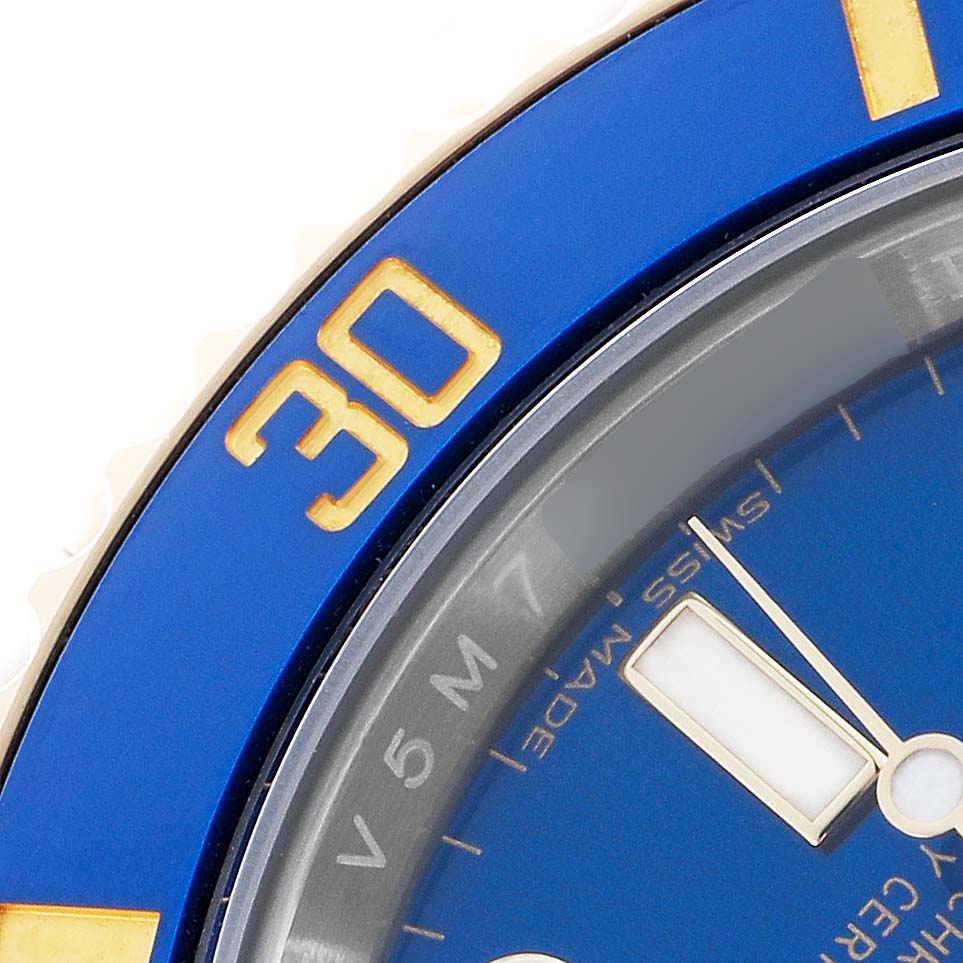 The image shows a close-up of the blue bezel with gold numbering and part of the dial of the Rolex Submariner 116613 Men's Steel and Gold (two tone) Blue Dial.