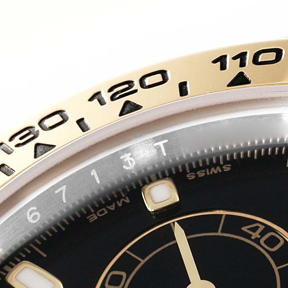 This close-up image shows part of the bezel and dial of a Rolex Daytona 116503 Men's Steel and Gold (two tone) Black Dial 116503 Men's Steel and Gold (two tone) Black Dial watch.