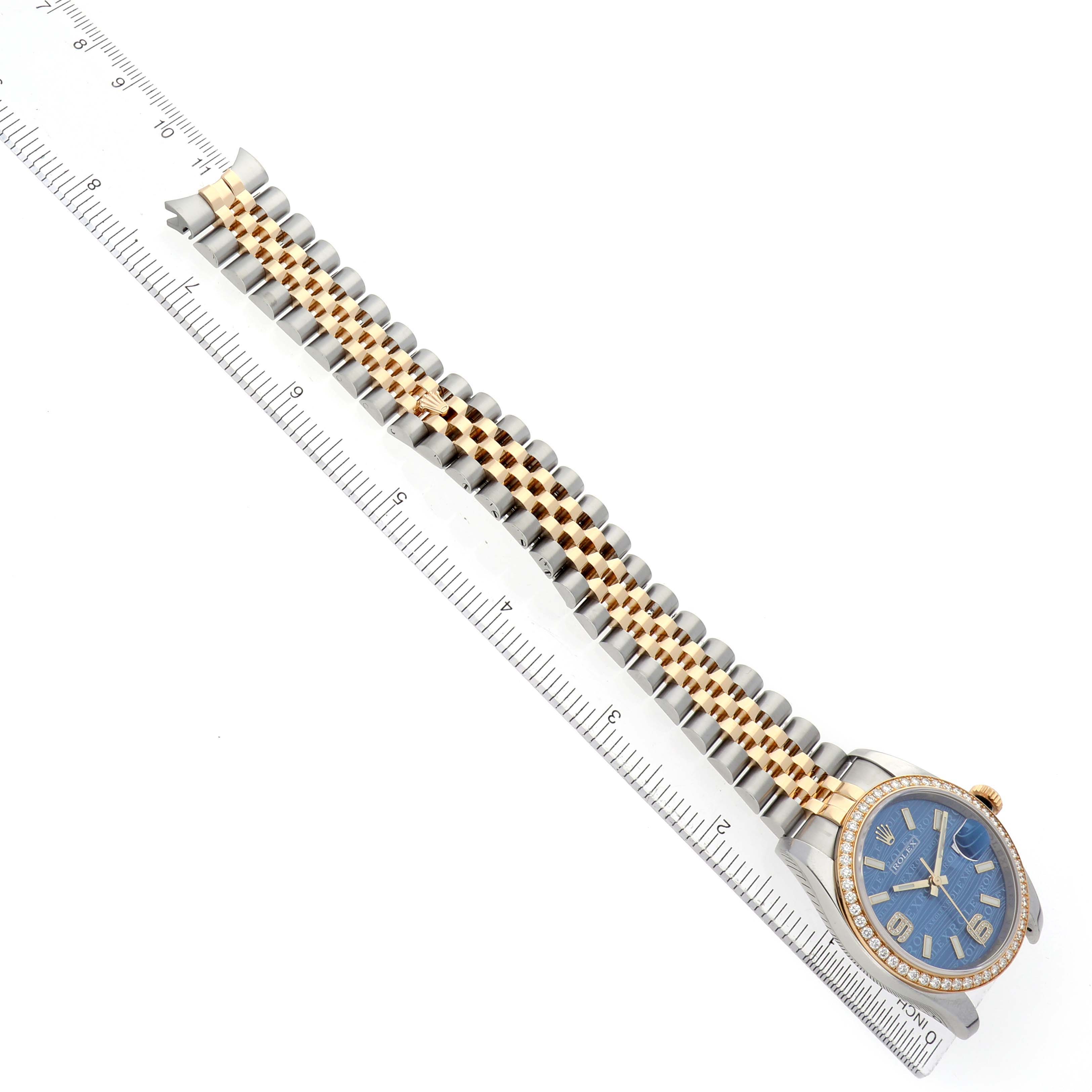 The Rolex Datejust 116243 Men's Steel and Gold (two tone) Blue Dial watch is shown at an angle showcasing the face, bezel, and full bracelet next to a ruler.