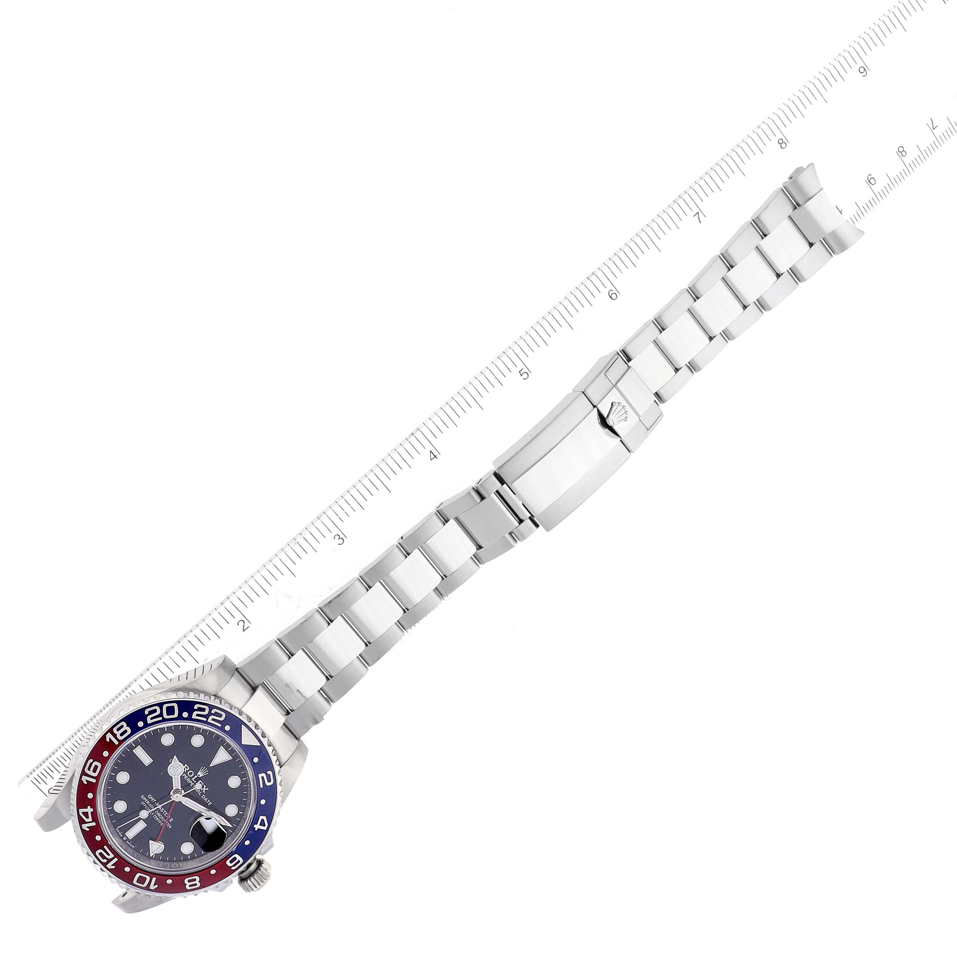 The image shows a top-down view of a Rolex GMT-Master 126710 Men
s Stainless Steel Black Dial 126710 Men
s Stainless Steel Black Dial watch with a two-tone bezel and a stainless steel bracelet extended next to a ruler.
