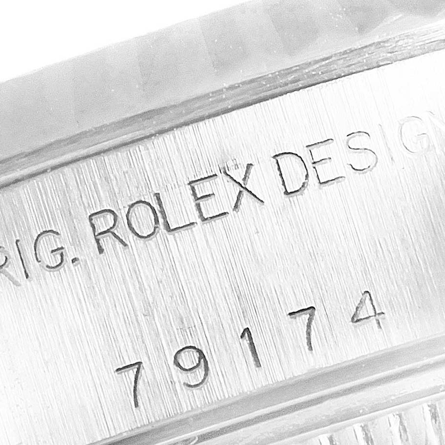 The image shows an engraved part of the Rolex Datejust 79174 Women
s Stainless Steel Silver Dial 79174 Women
s Stainless Steel Silver Dial model, focusing on the serial number and "ROLEX DESIGN" text.