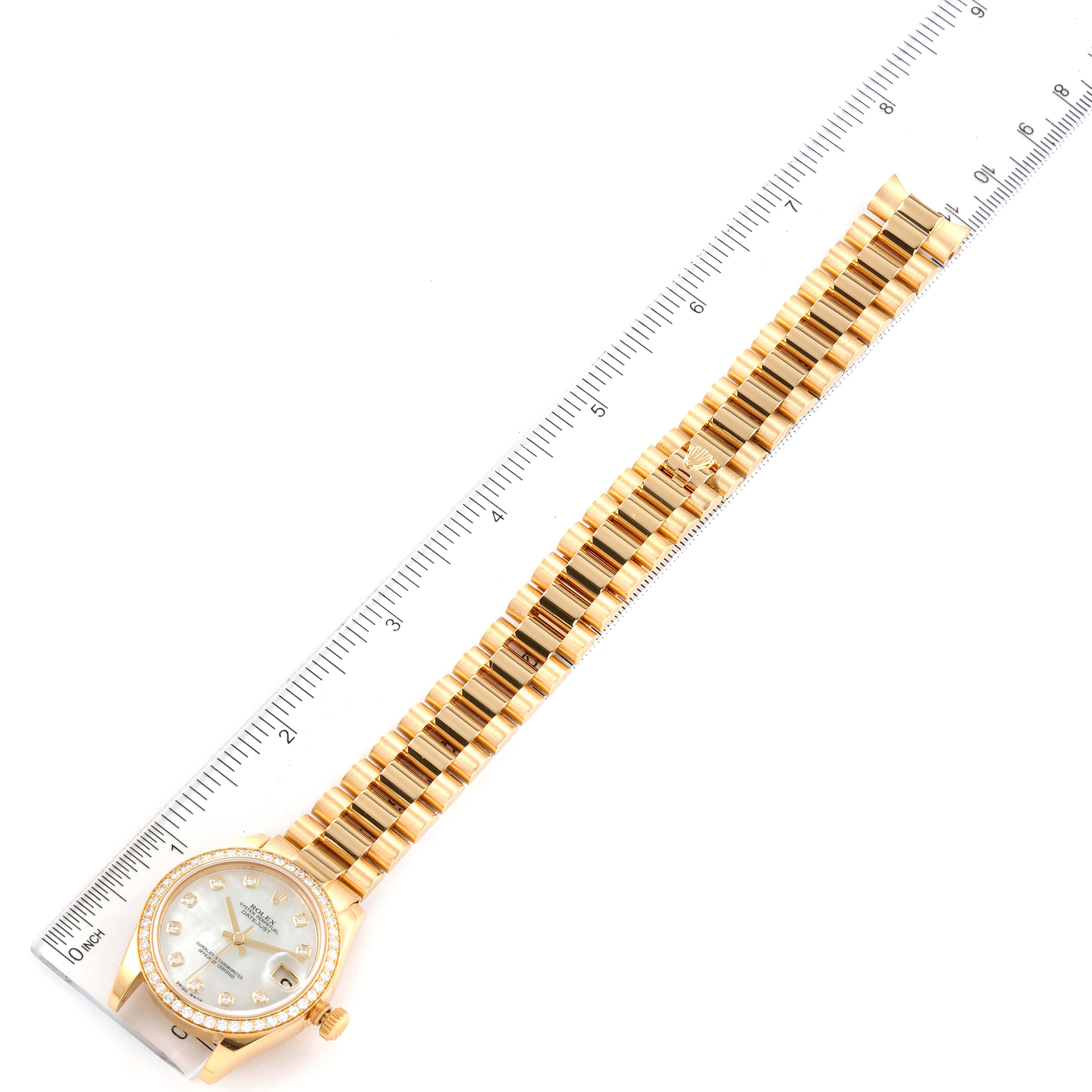 The image shows a Rolex President 178288 Women
s Yellow Gold Mother of Pearl Dial 178288 Women
s Yellow Gold Mother of Pearl Dial model watch laid flat next to a ruler, highlighting its bracelet and dial.