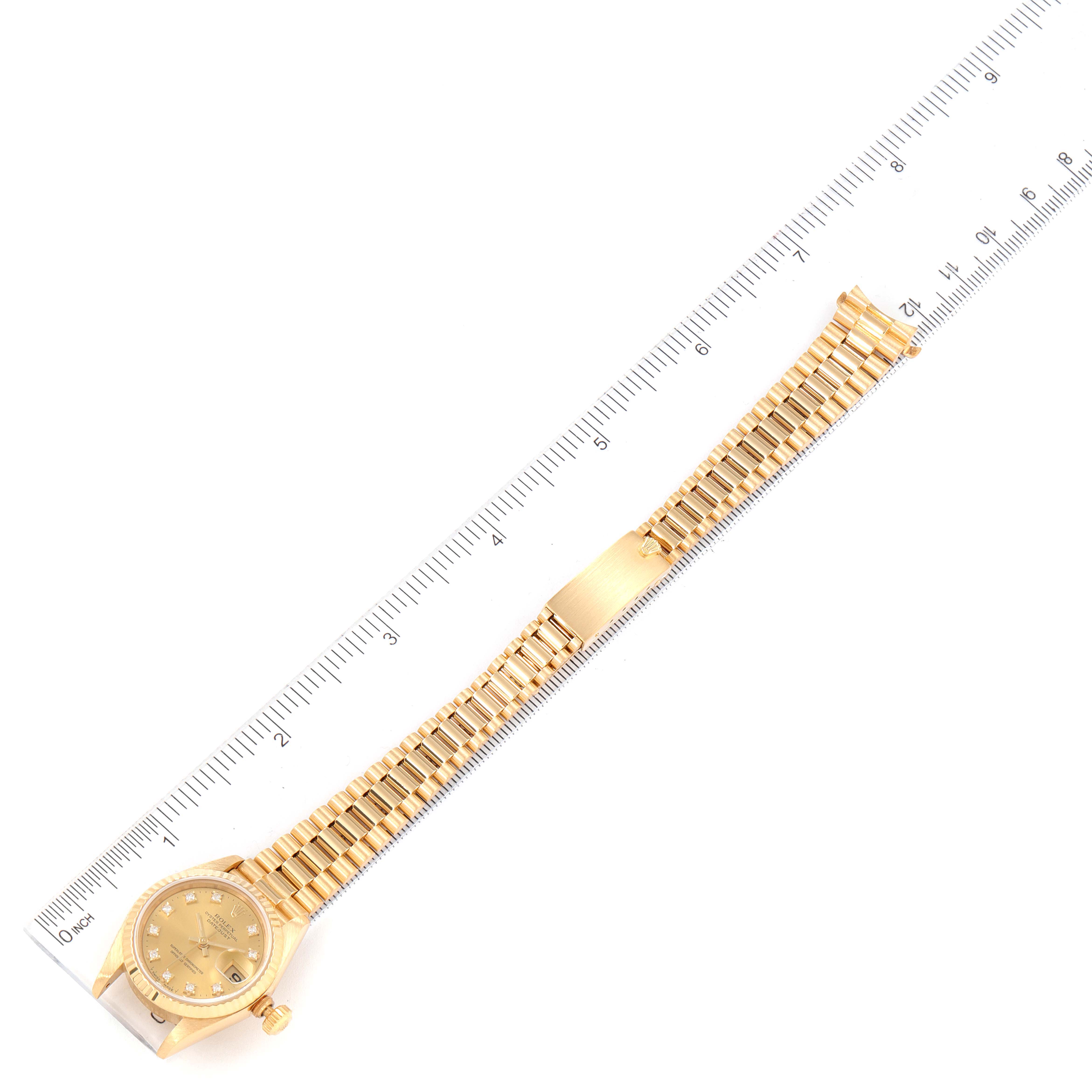 The image shows a Rolex President 69178 Women
s Yellow Gold Champagne Dial 69178 Women
s Yellow Gold Champagne Dial model watch laid flat with its bracelet extended, alongside a ruler for measurement.