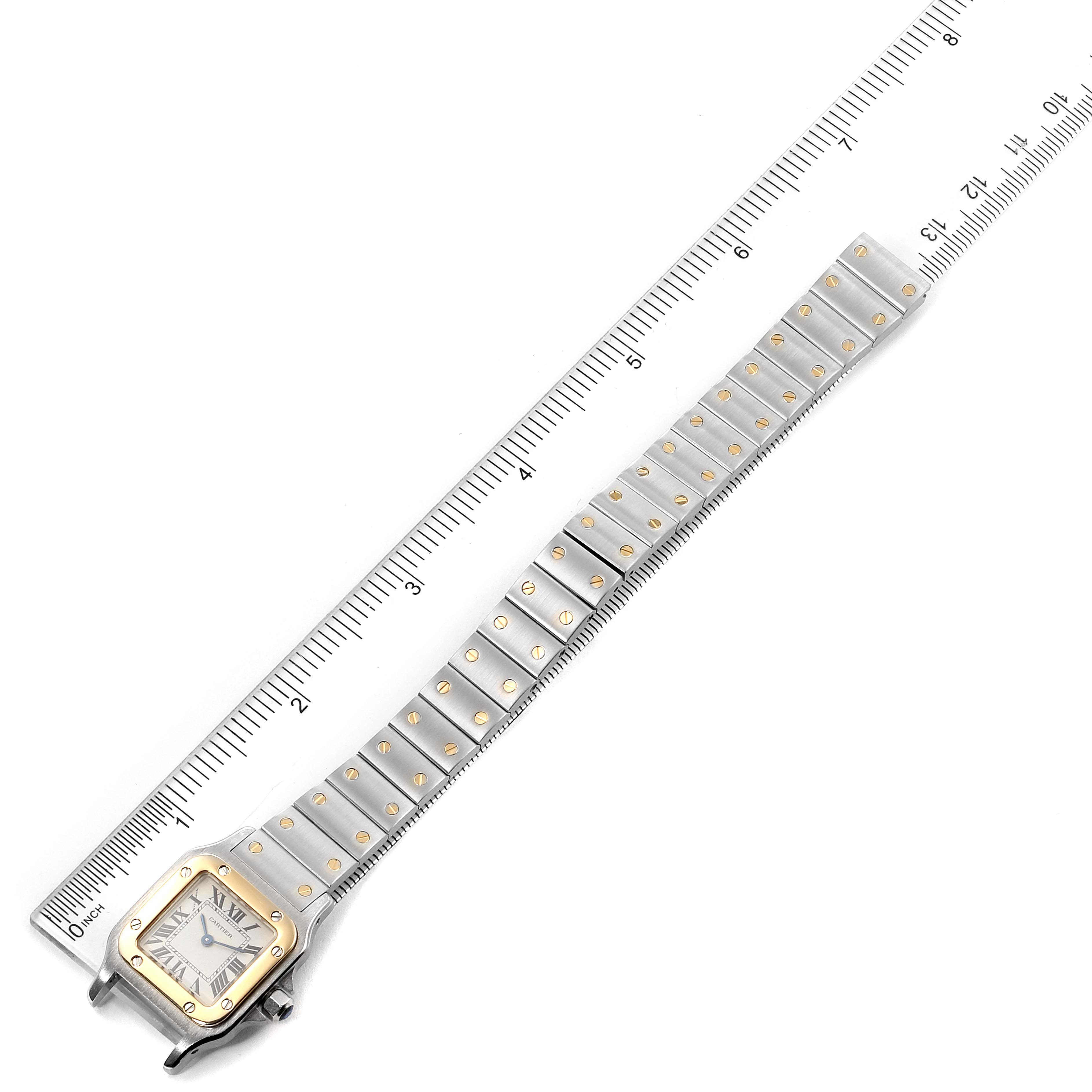 This image shows a Santos model watch by Cartier laid flat alongside a ruler, displaying its face and full bracelet.