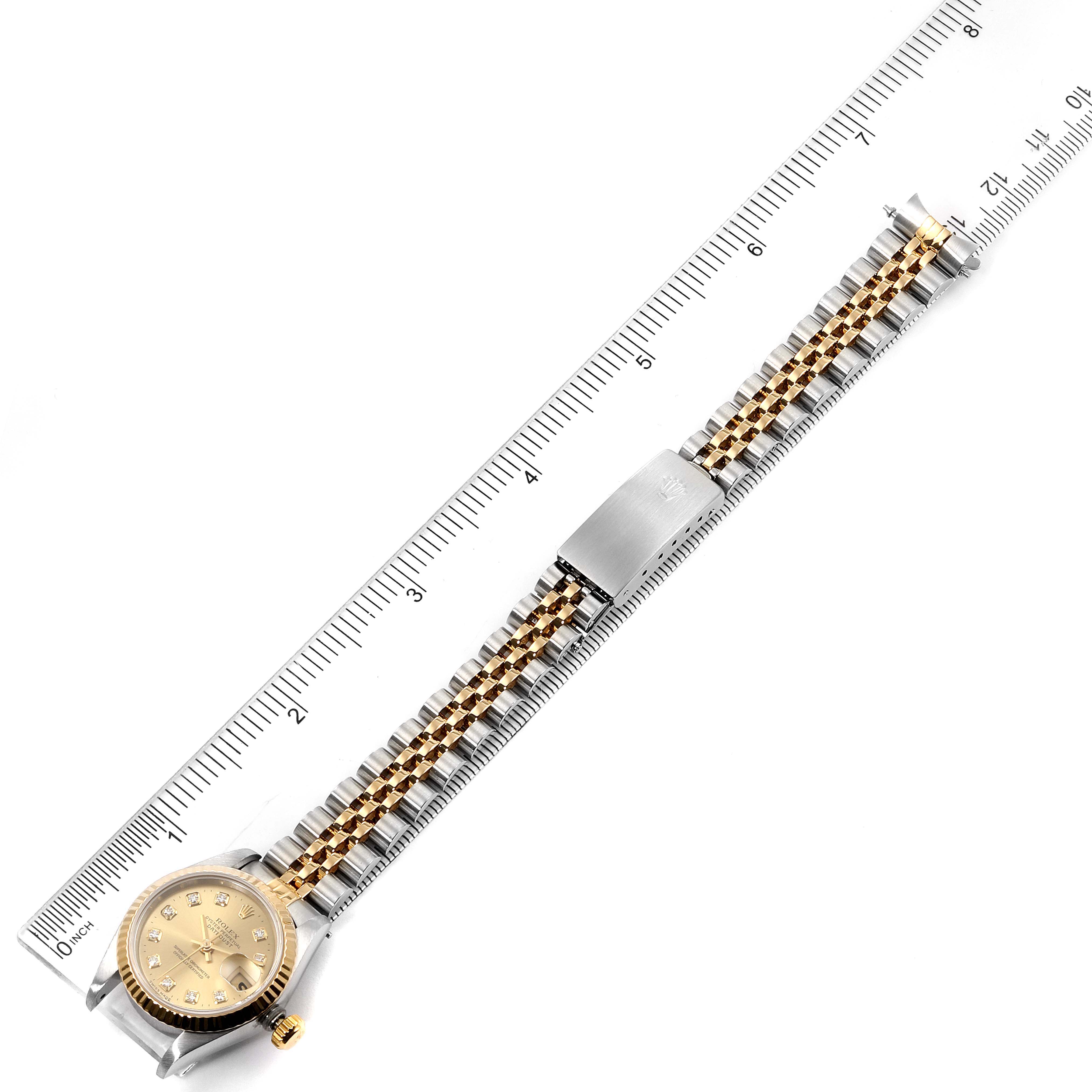 The image shows a Rolex Datejust 69173 Women
s Steel and Gold (two tone) Champagne Dial 69173 Women
s Steel and Gold (two tone) Champagne Dial watch lying flat with a ruler, highlighting its bracelet and face.