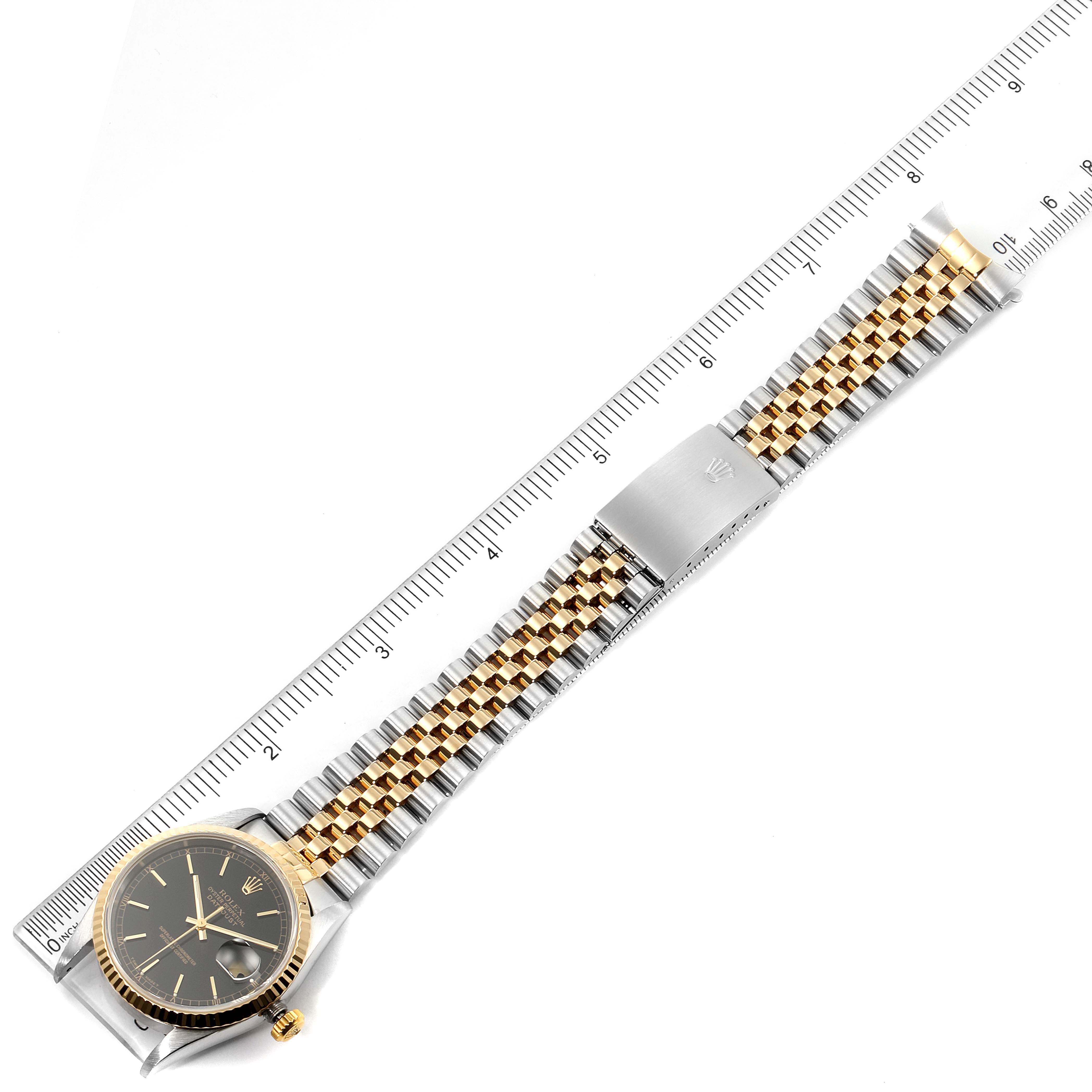 The image shows a top-down view of a Rolex Datejust 16233 Men's Steel and Gold (two tone) Black Dial 16233 Men's Steel and Gold (two tone) Black Dial watch, displaying the face, band, and clasp with a ruler for scale.