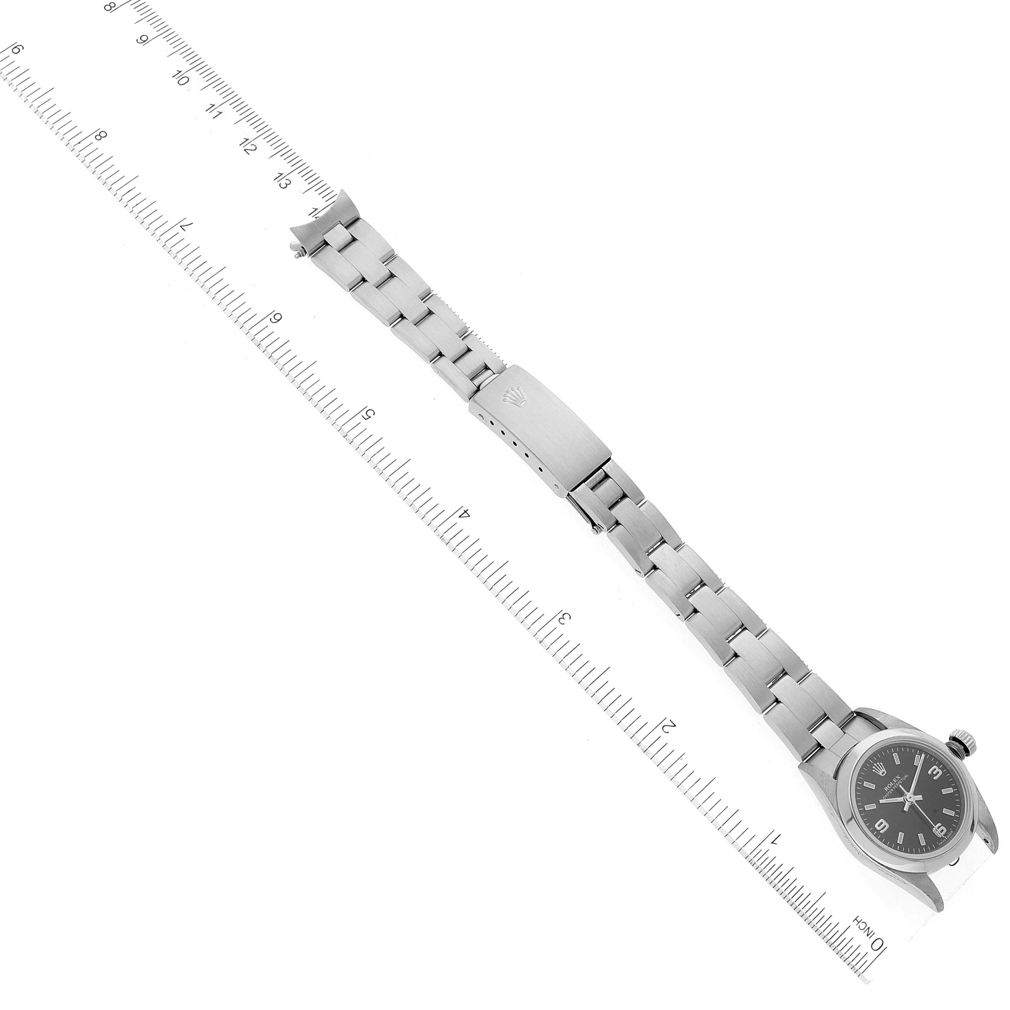 The image shows an overhead view of a Rolex Oyster Perpetual 76080 Women's Stainless Steel Black Dial 76080 Women's Stainless Steel Black Dial watch, displaying its stainless steel bracelet and dial next to a ruler.
