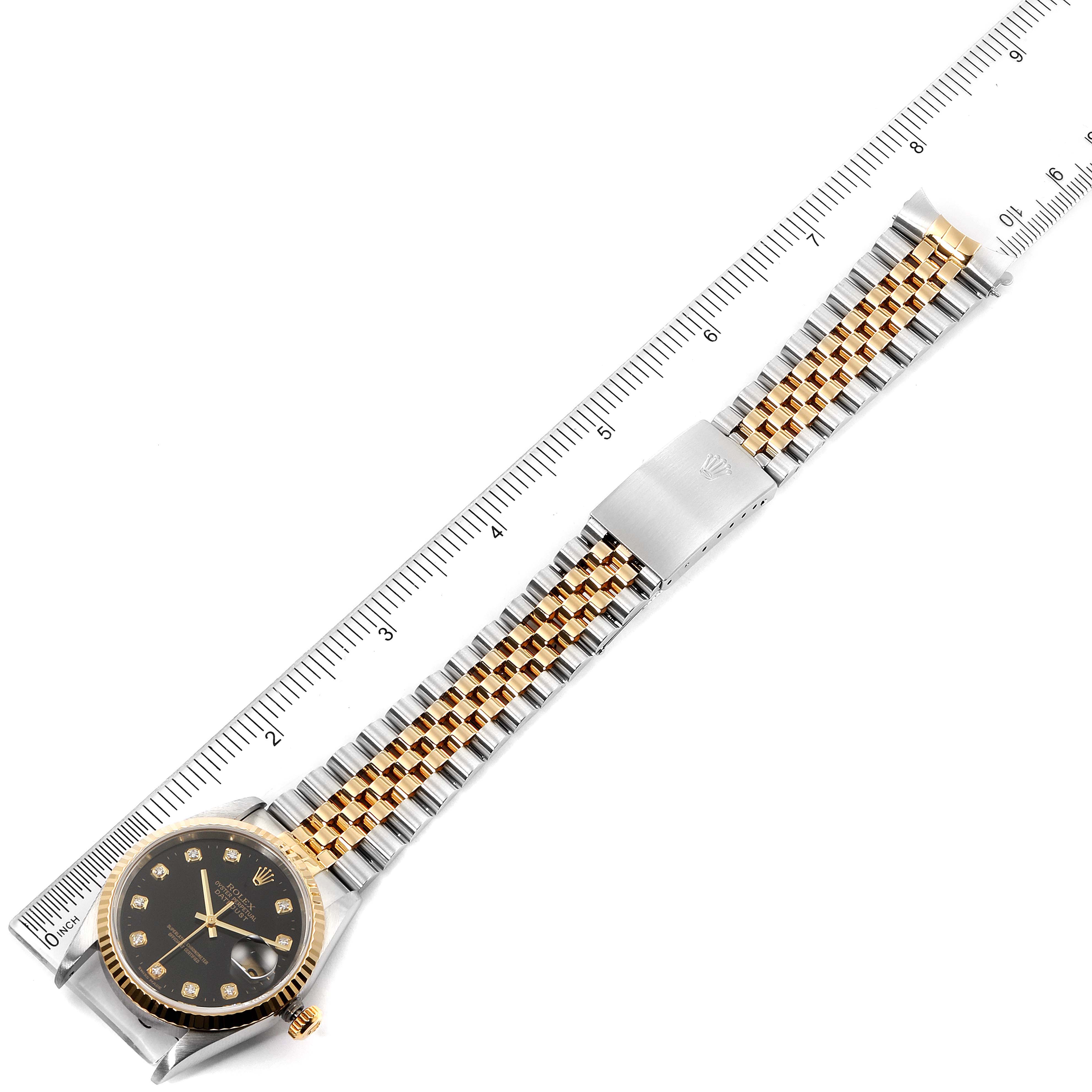 The image shows a top-down view of a Rolex Datejust 16233 Men's Steel and Gold (two tone) Black Dial 16233 Men's Steel and Gold (two tone) Black Dial model, displaying its entire band, face, and clasp next to a ruler.