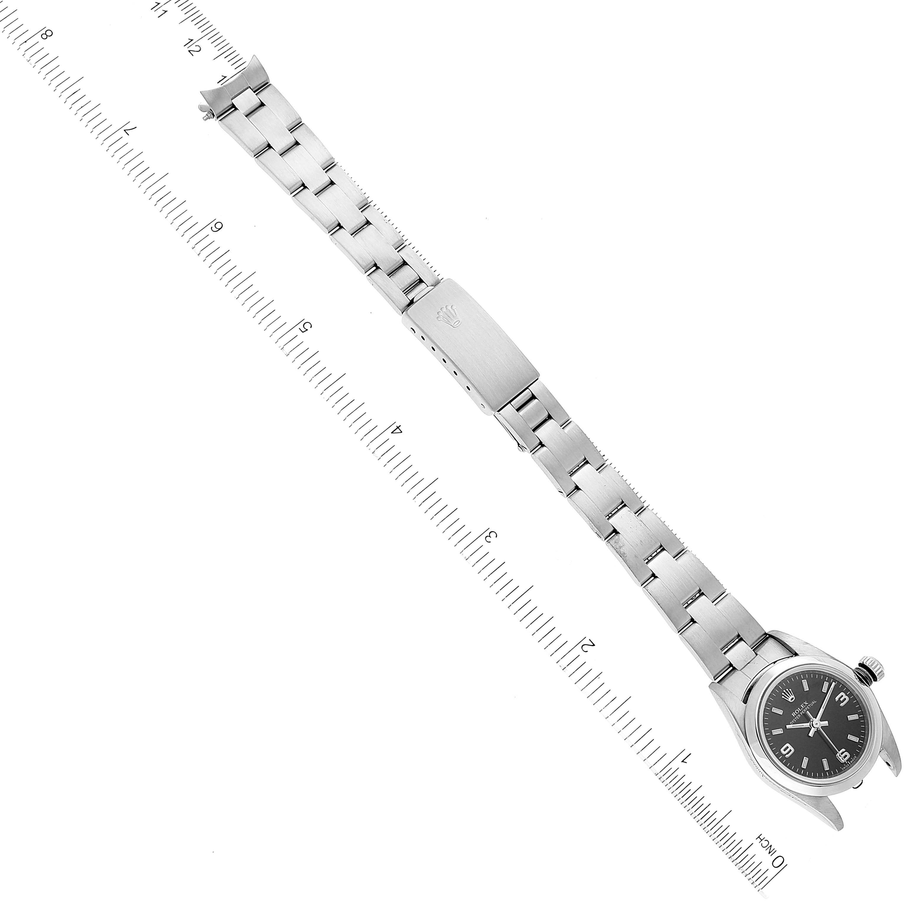 The image shows a Rolex Oyster Perpetual 76080 Women's Stainless Steel Black Dial 76080 Women's Stainless Steel Black Dial watch laid flat, displaying the face, bracelet, and clasp, alongside a ruler for scale.