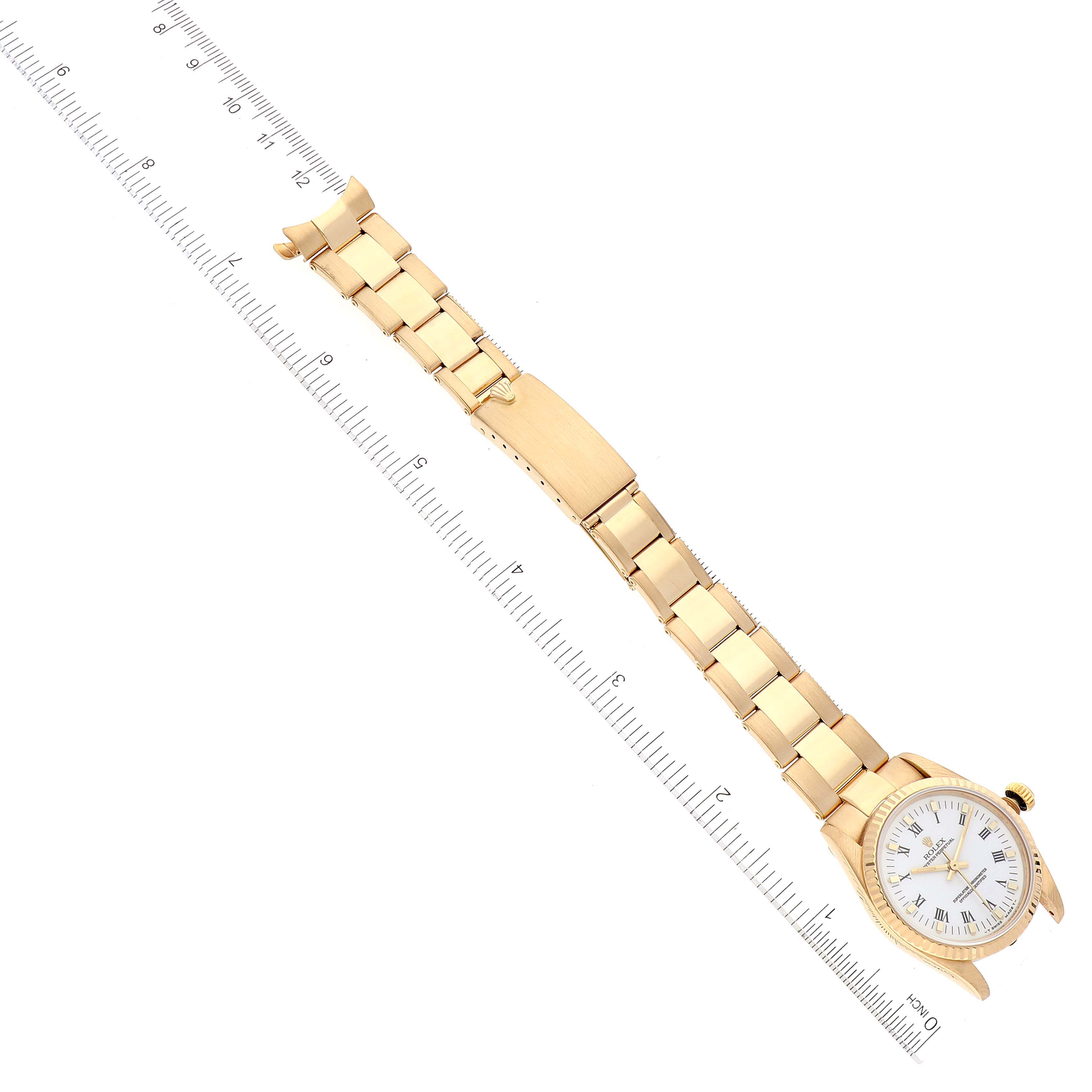 The image shows a Rolex President 67518 Women
s Yellow Gold White Dial 67518 Women
s Yellow Gold White Dial model watch from a top-down angle, displaying the watch face, bracelet, and clasp, next to a measuring ruler.