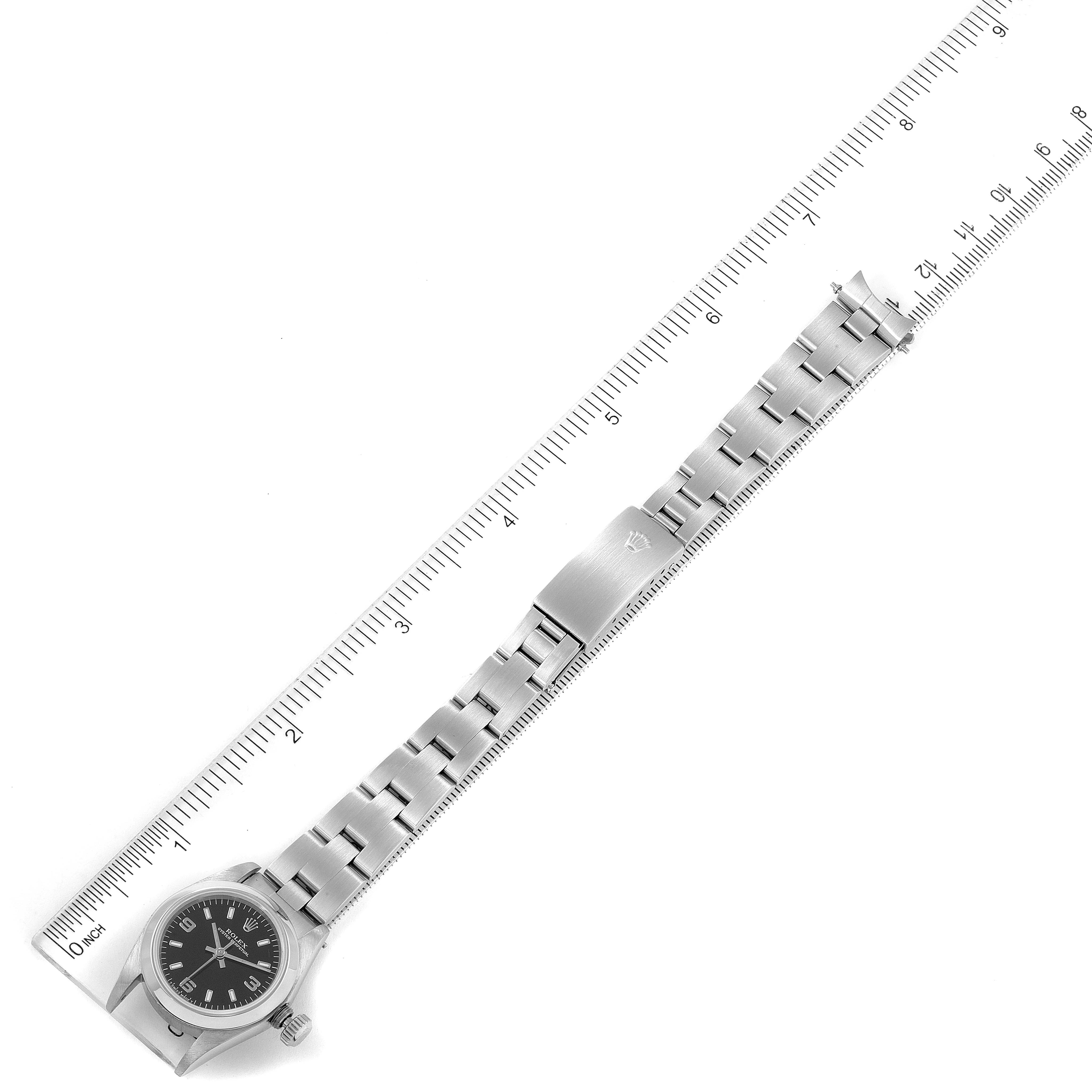 The Rolex Oyster Perpetual 67180 Women's Stainless Steel Black Dial 67180 Women's Stainless Steel Black Dial watch is shown laid out flat next to a ruler, displaying the face, case, bracelet, and clasp.