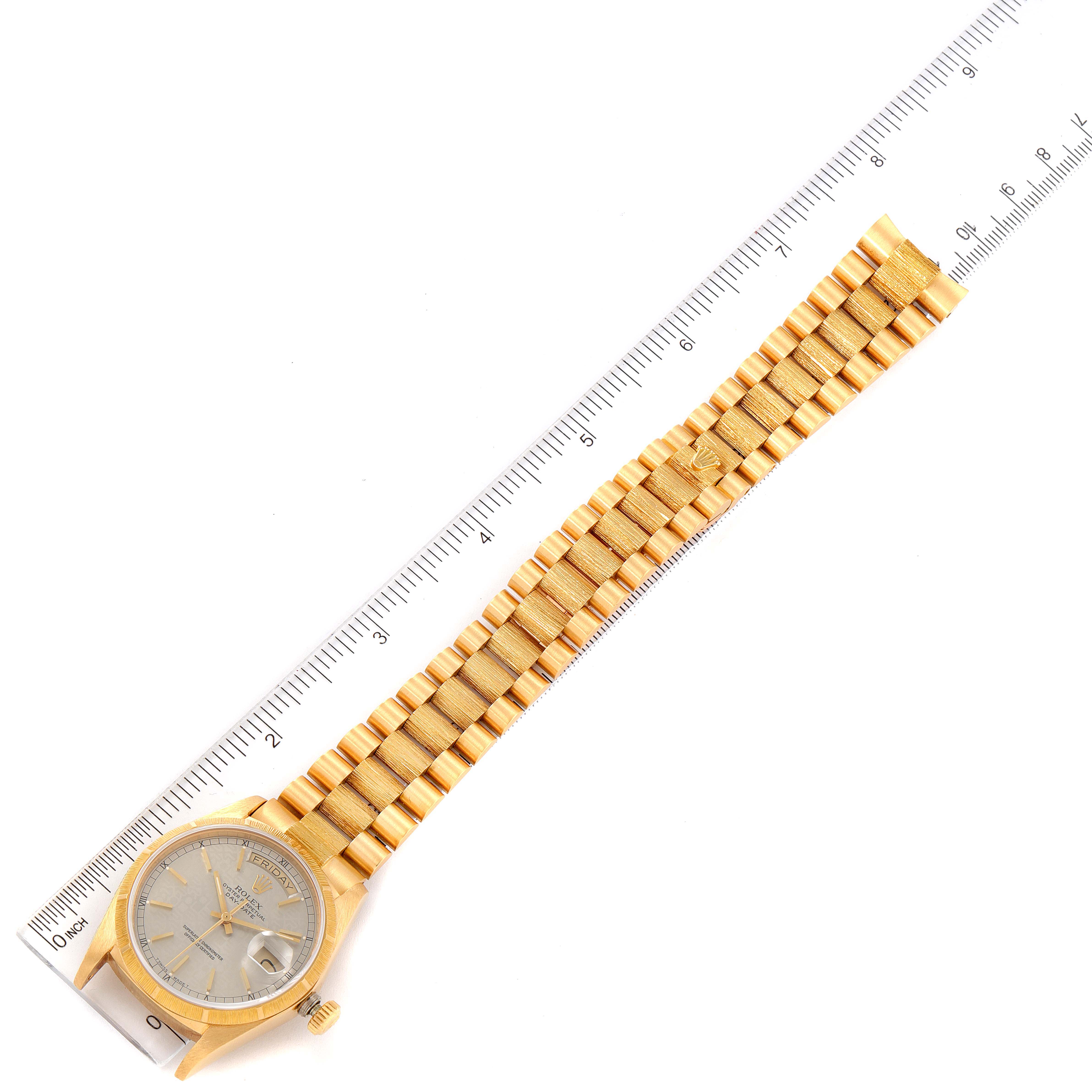 The Rolex President 18078 Men
s Yellow Gold Silver Dial 18078 Men
s Yellow Gold Silver Dial model watch is shown from a top angle alongside a ruler, displaying its face, bracelet, and part of the clasp.