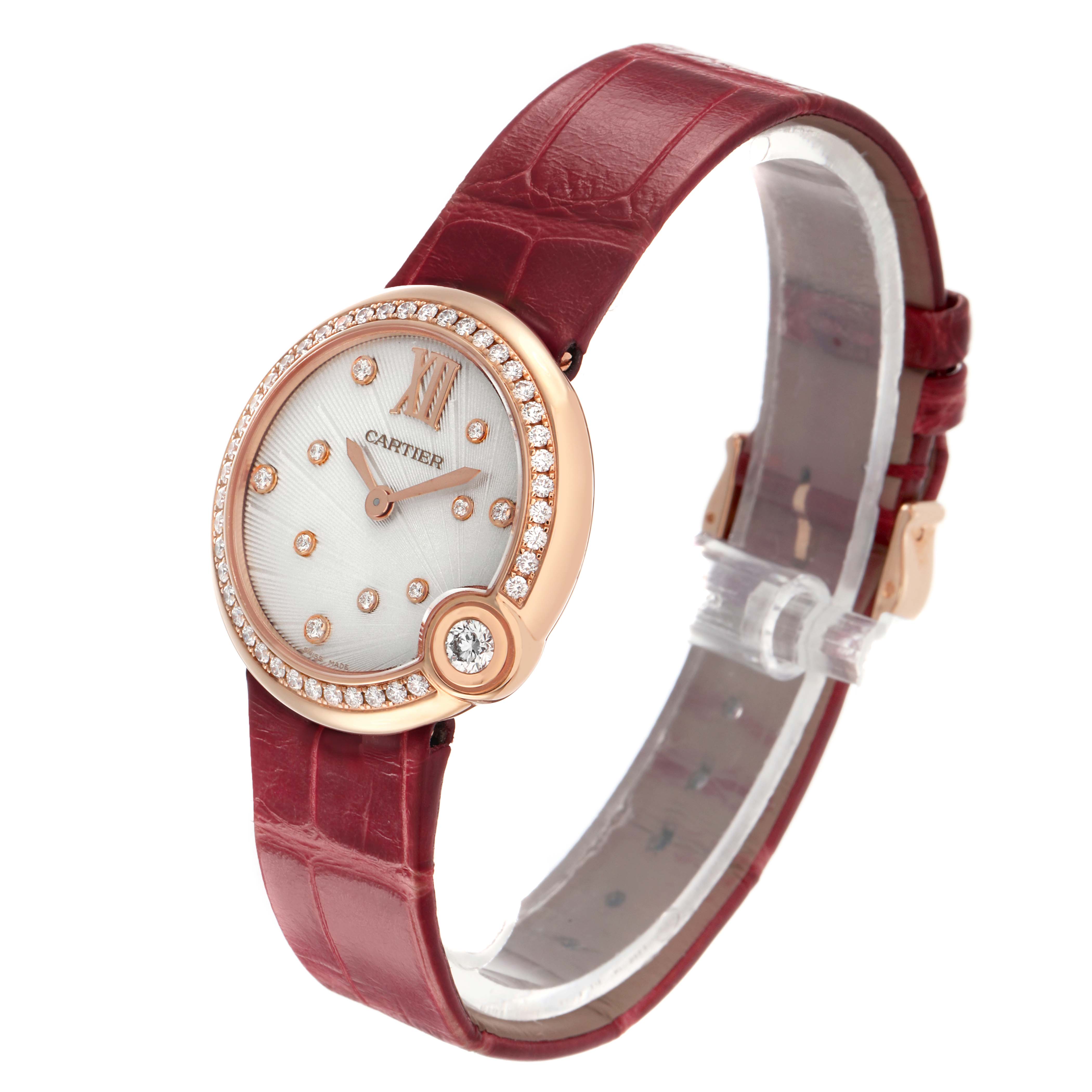 The Cartier Ballon Blanc WJBL0012 Women's Rose Gold Silver Dial watch is shown in a three-quarter view, highlighting its round case, diamond bezel, and red strap.