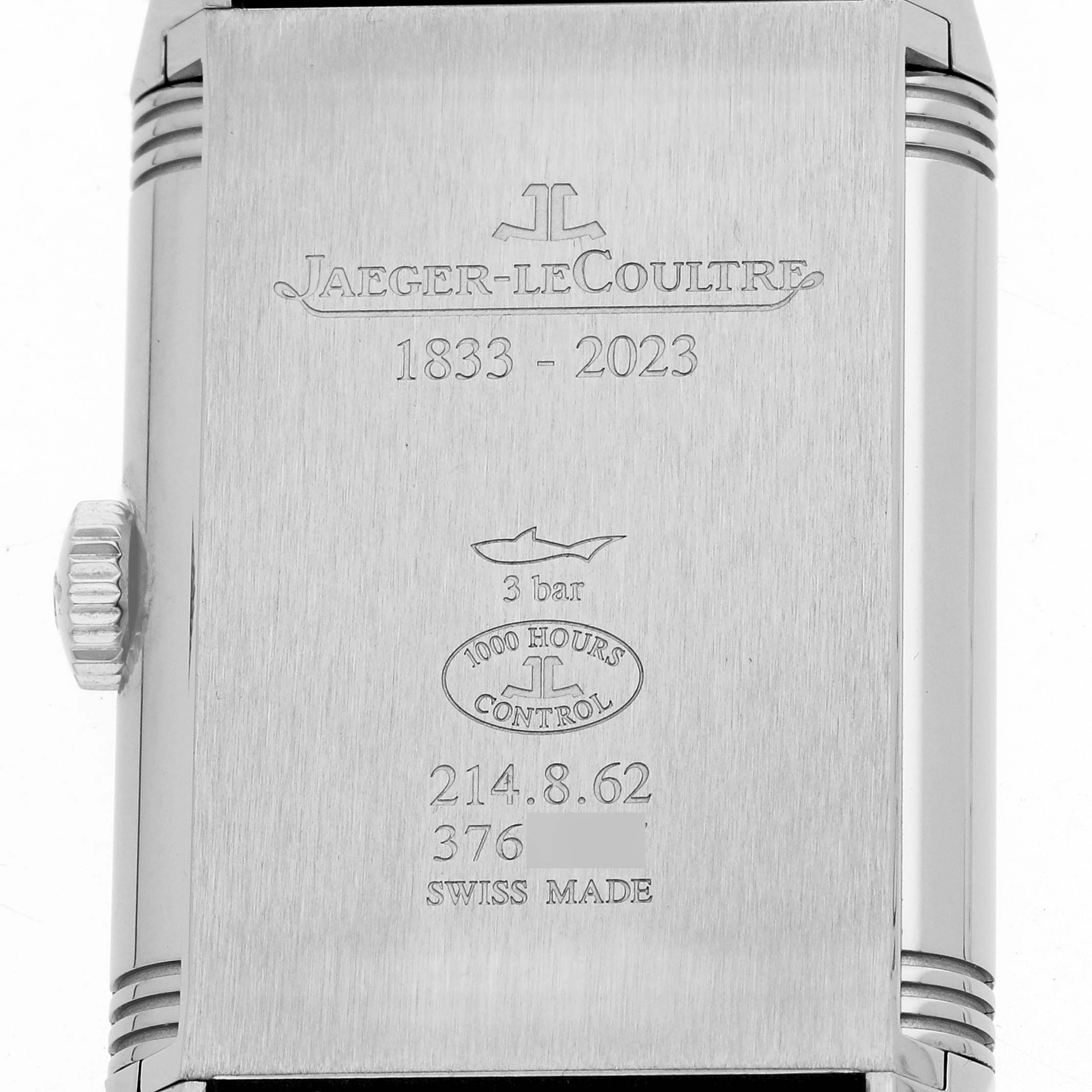 The image shows the back of a Jaeger-LeCoultre Reverso watch with engraved details and the crown visible on the side.