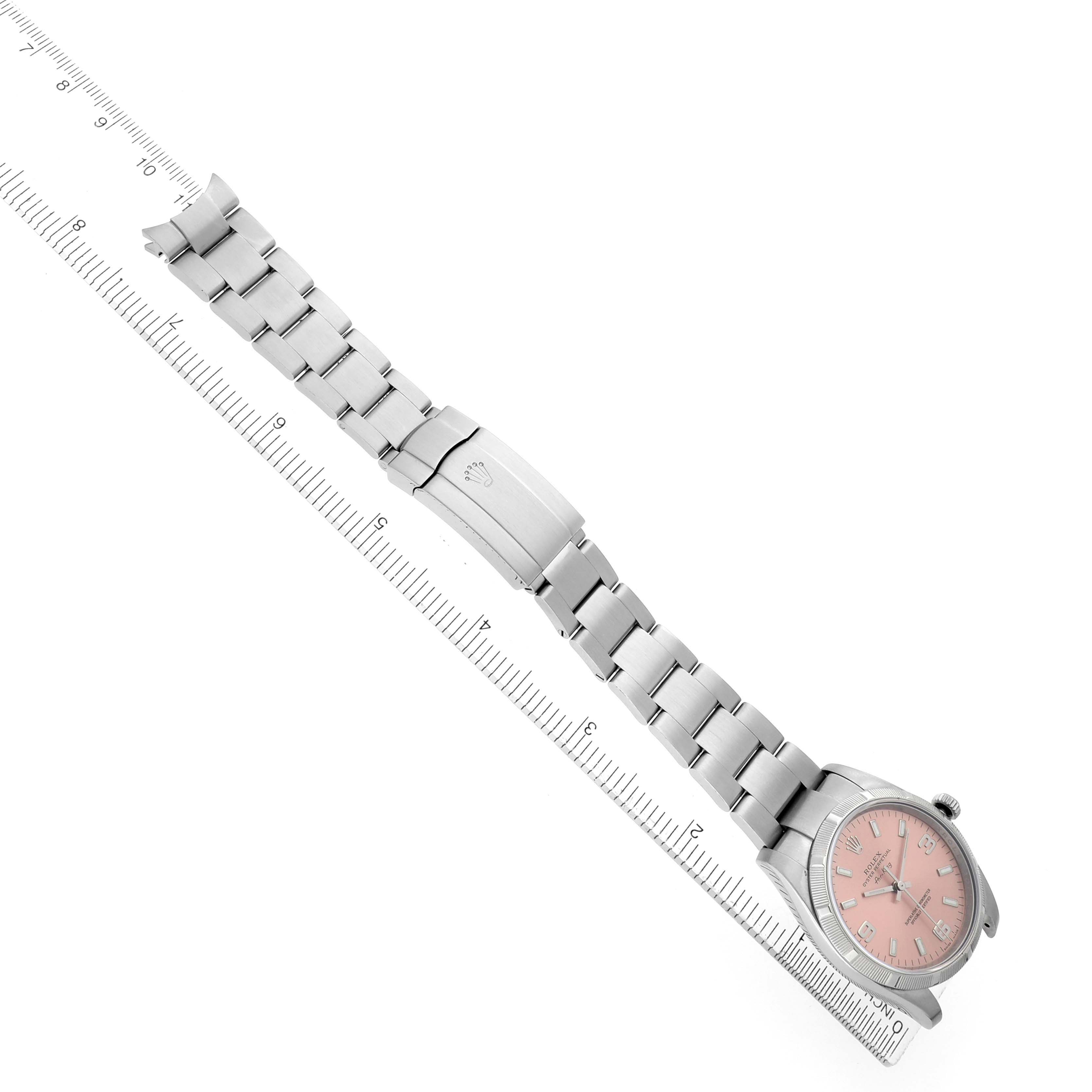 The image shows a Rolex Air-King 114210 Men's Stainless Steel Pink Dial watch at an angle highlighting its full bracelet and pink dial on a ruler scale backdrop.