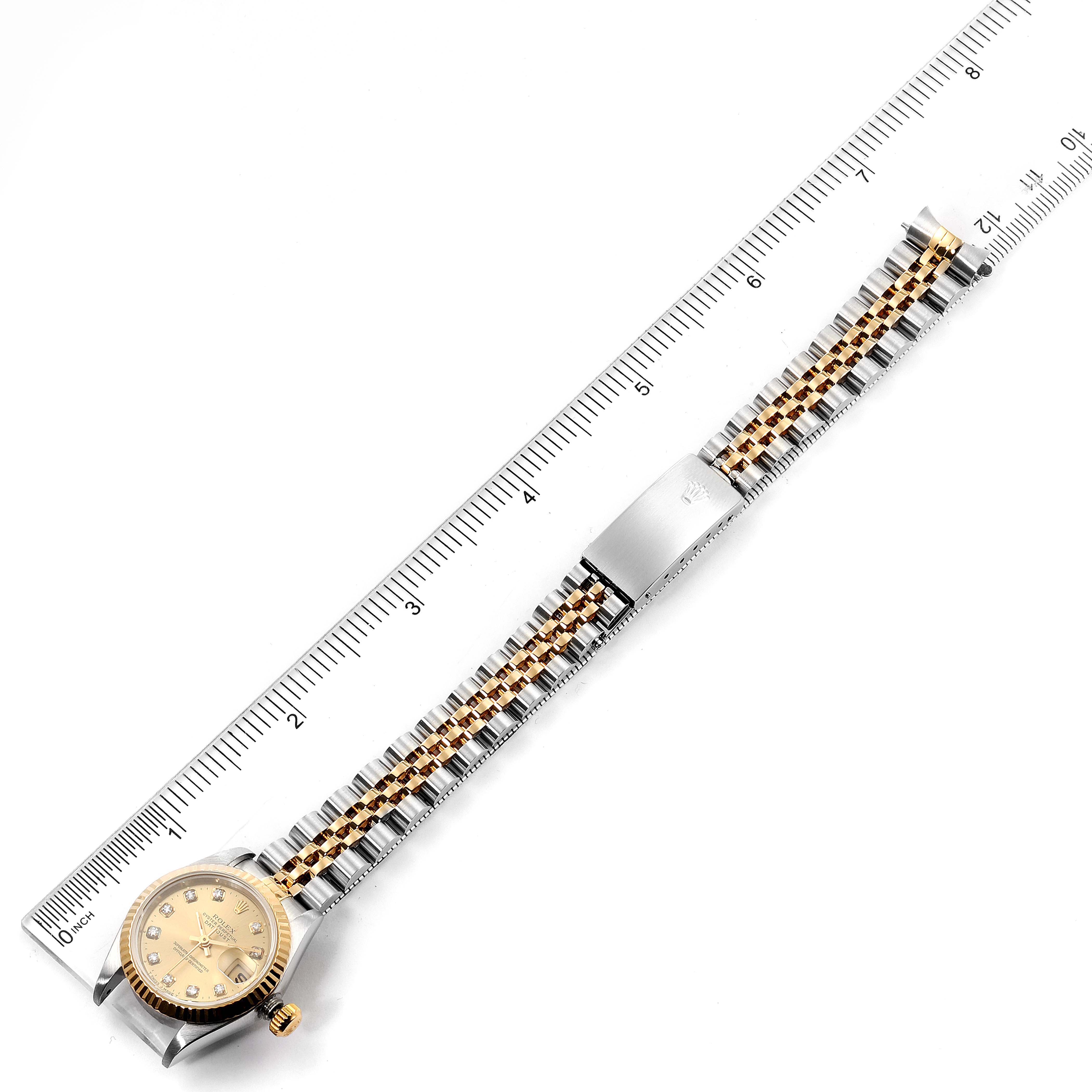 The image shows a Rolex Datejust 69173 Women
s Steel and Gold (two tone) Champagne Dial 69173 Women
s Steel and Gold (two tone) Champagne Dial watch laid flat alongside a ruler, displaying the face, band, and clasp.