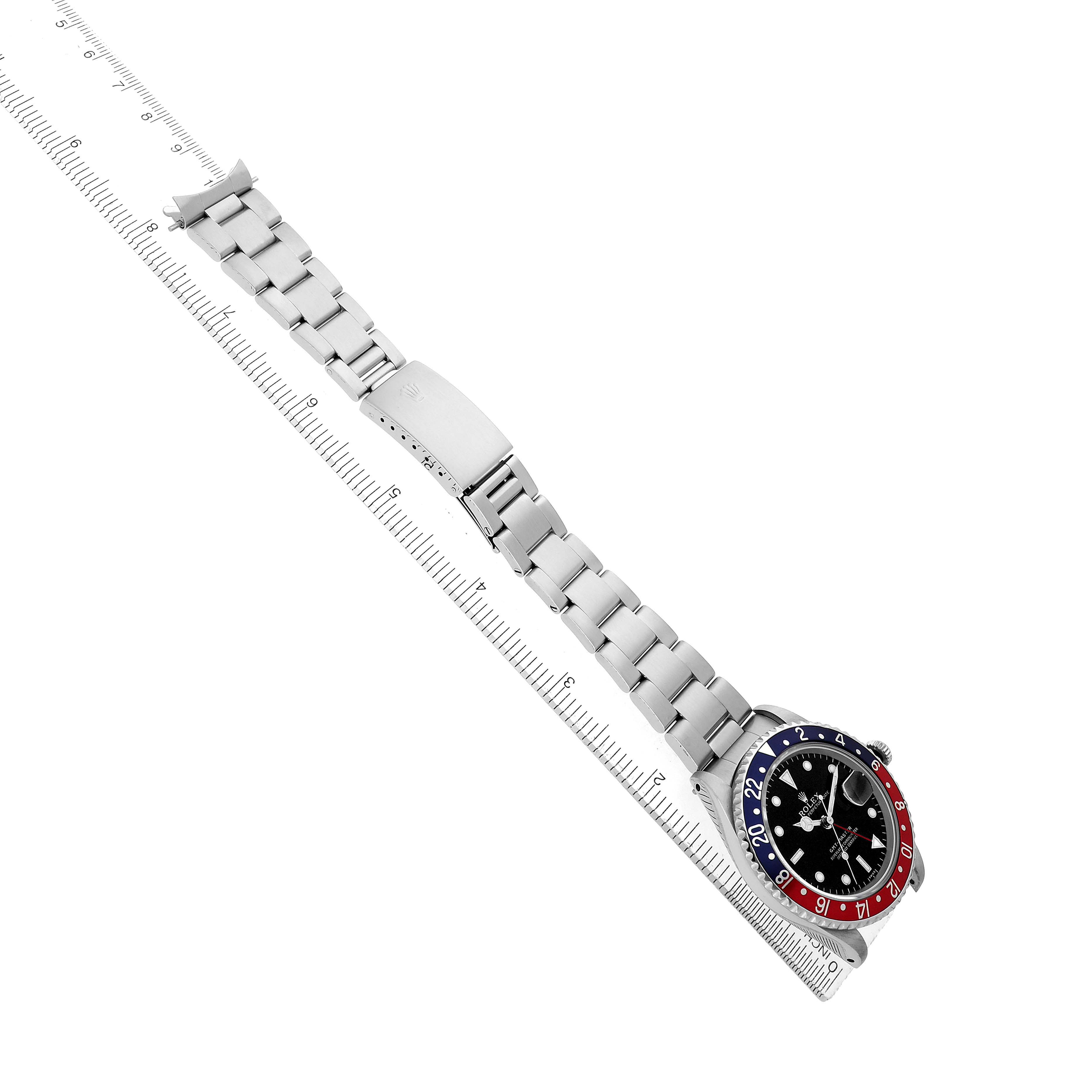 The Rolex GMT-Master 16700 Men's Stainless Steel Black Dial watch is shown from a top angle, displaying its bracelet and bezel on a ruler.