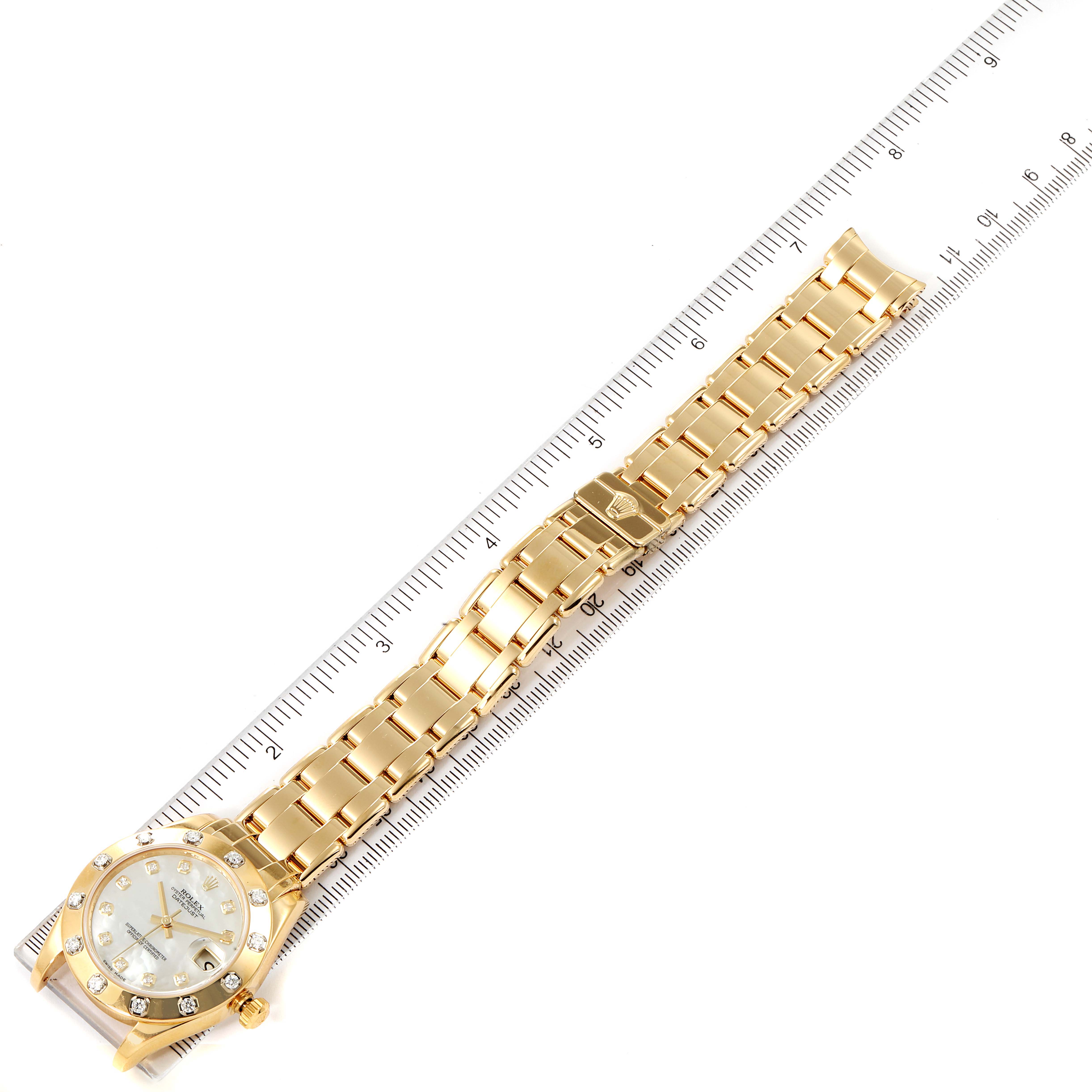 This image shows a Rolex Pearlmaster 81318 Women's Yellow Gold Mother of Pearl Dial 81318 Women's Yellow Gold Mother of Pearl Dial watch laid flat alongside a ruler, displaying its gold bracelet and face from a top view.