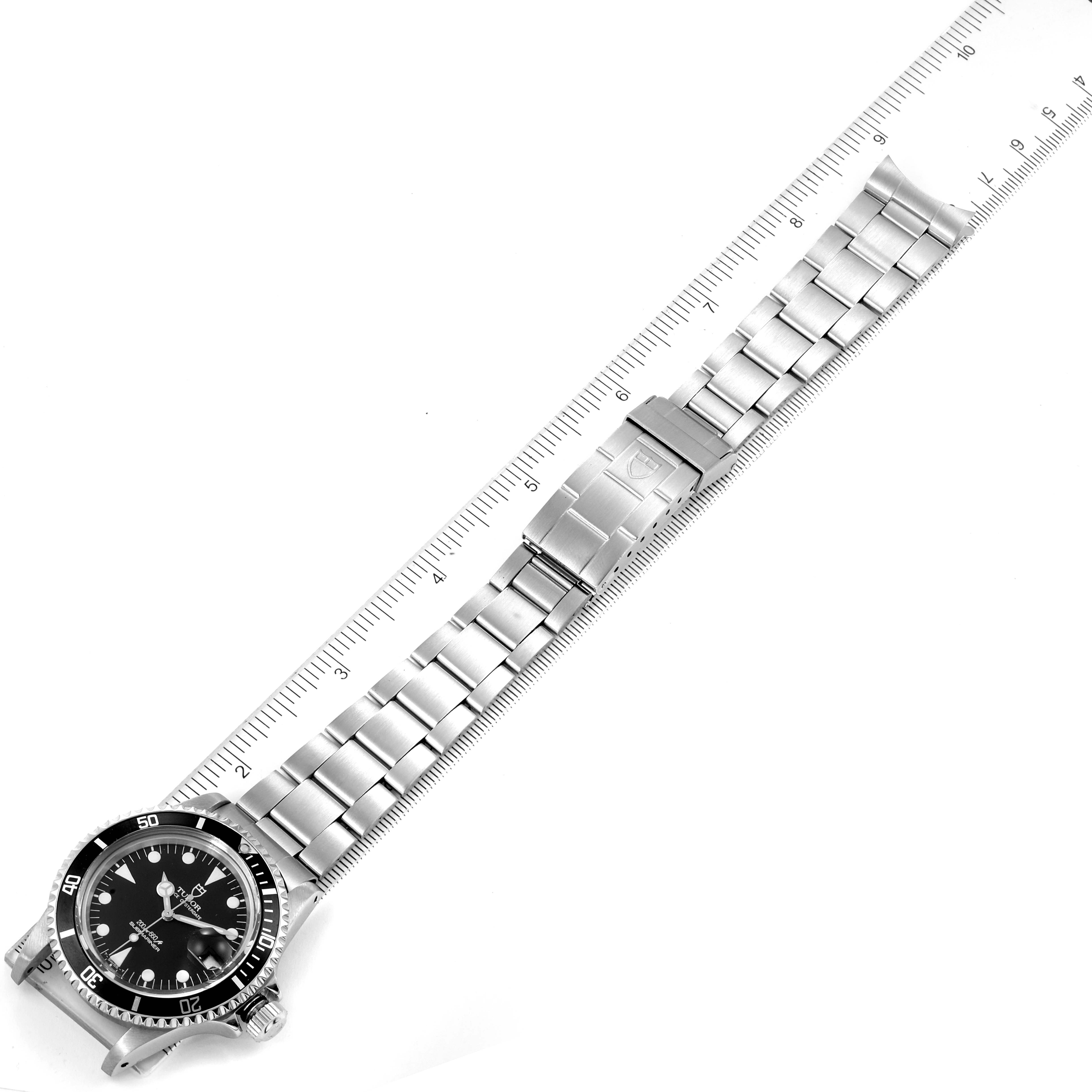This image shows a Tudor Submariner 79090 Men
s Stainless Steel Black Dial 79090 Men
s Stainless Steel Black Dial watch laid flat with its bracelet extended alongside a ruler for measurement.