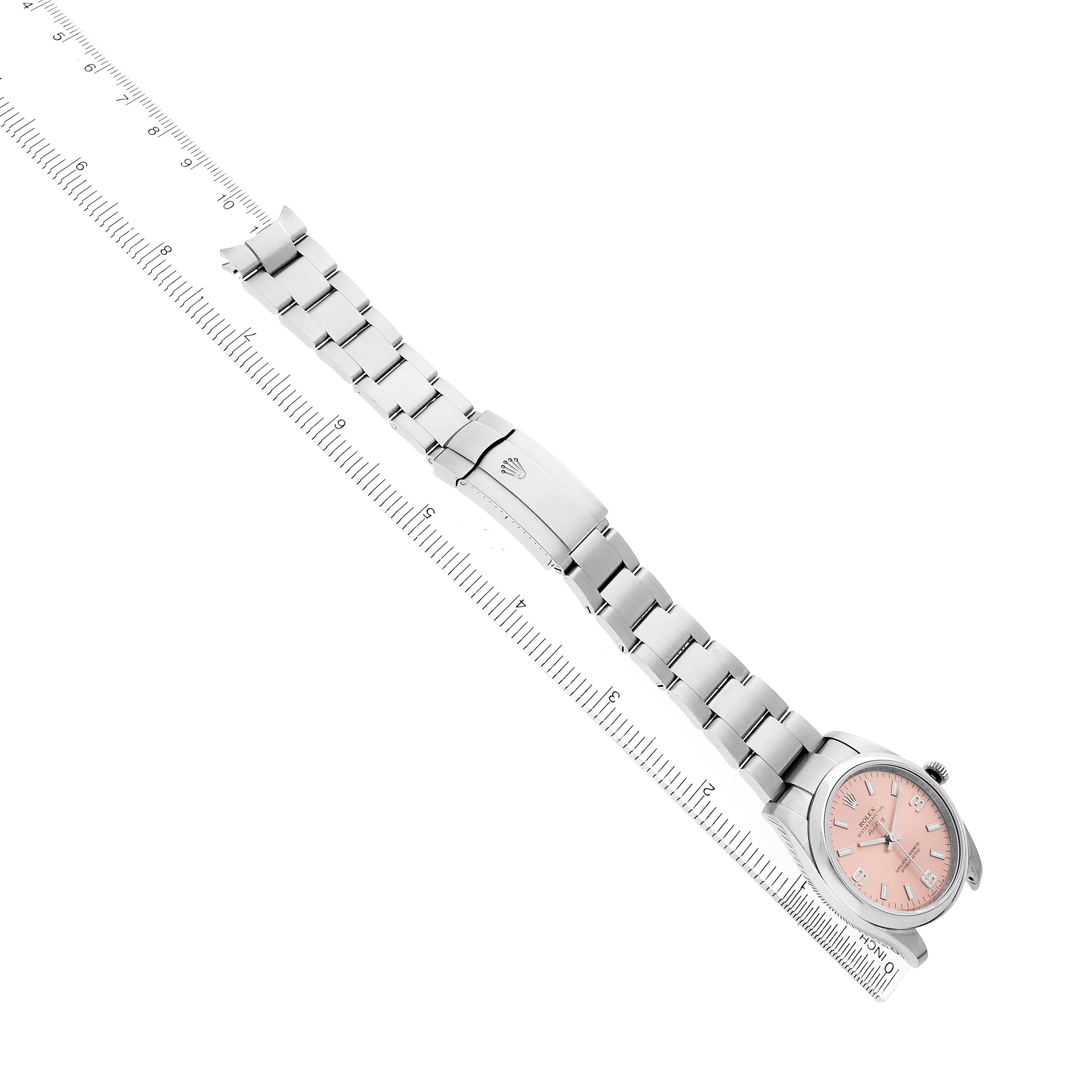 The Rolex Air-King 114200 Men's Stainless Steel Pink Dial watch is shown at a diagonal angle, displaying its pink dial and metal bracelet fully extended alongside a ruler.