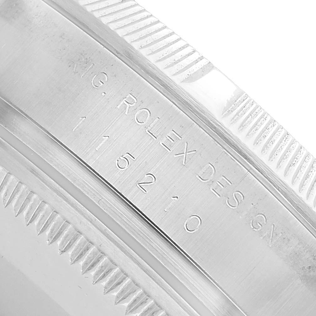 The image shows a close-up of the Rolex Date 115210 Men's Stainless Steel White Dial model's case side, highlighting the engraved model number and design details.