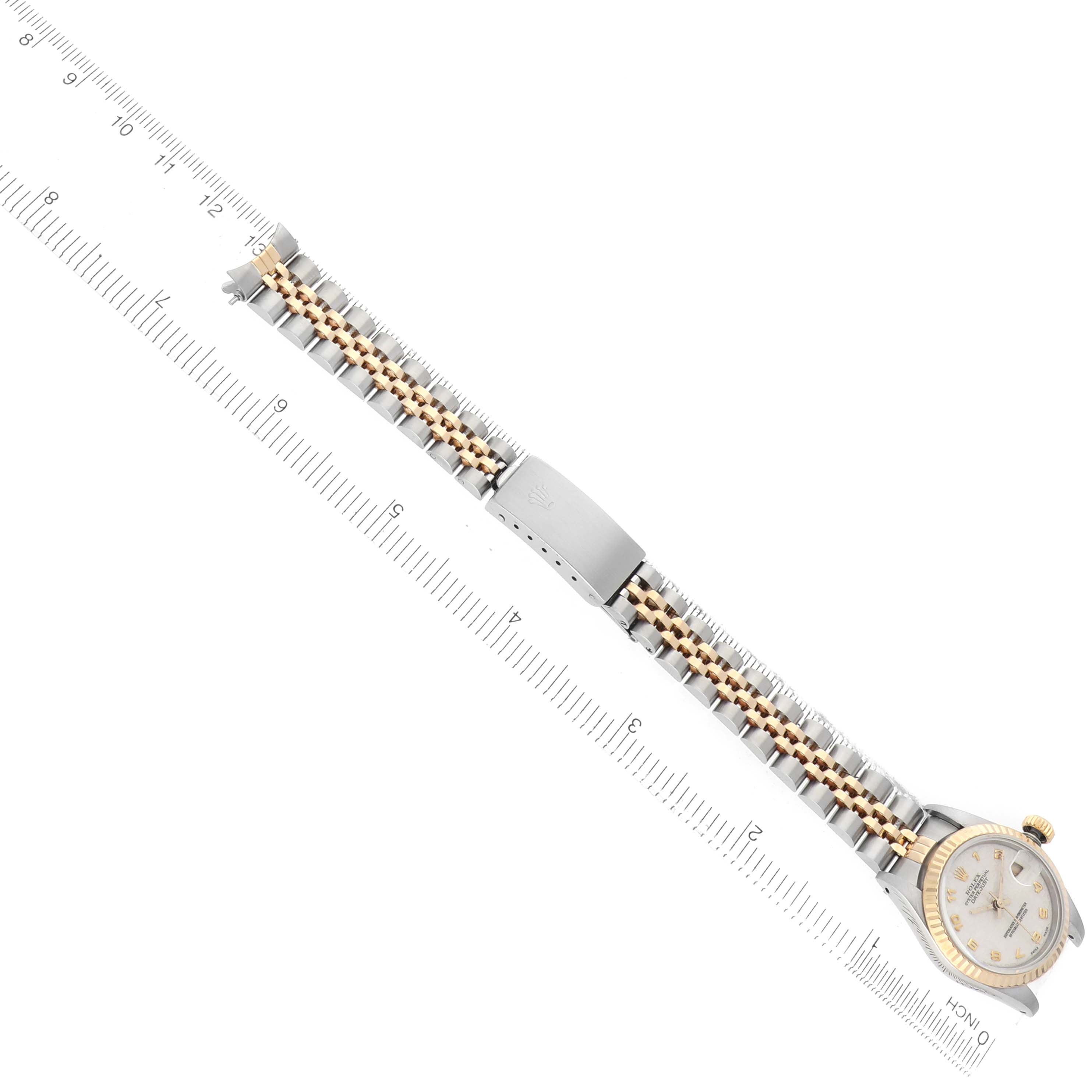 The Rolex Datejust 69173 Women's Steel and Gold (two tone) White Dial watch is shown from a top angle, highlighting the bracelet and clasp alongside a measuring ruler.