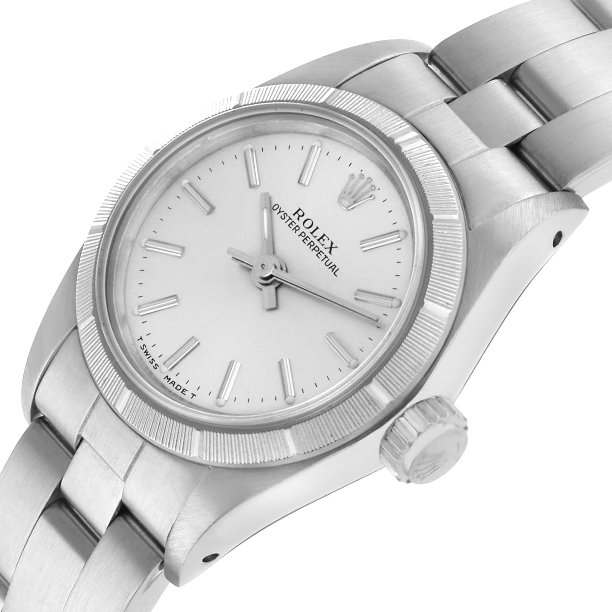 The Rolex Oyster Perpetual 67230 Women's Stainless Steel Silver Dial watch is shown at a tilted angle, highlighting the dial, bezel, crown, and part of the bracelet.