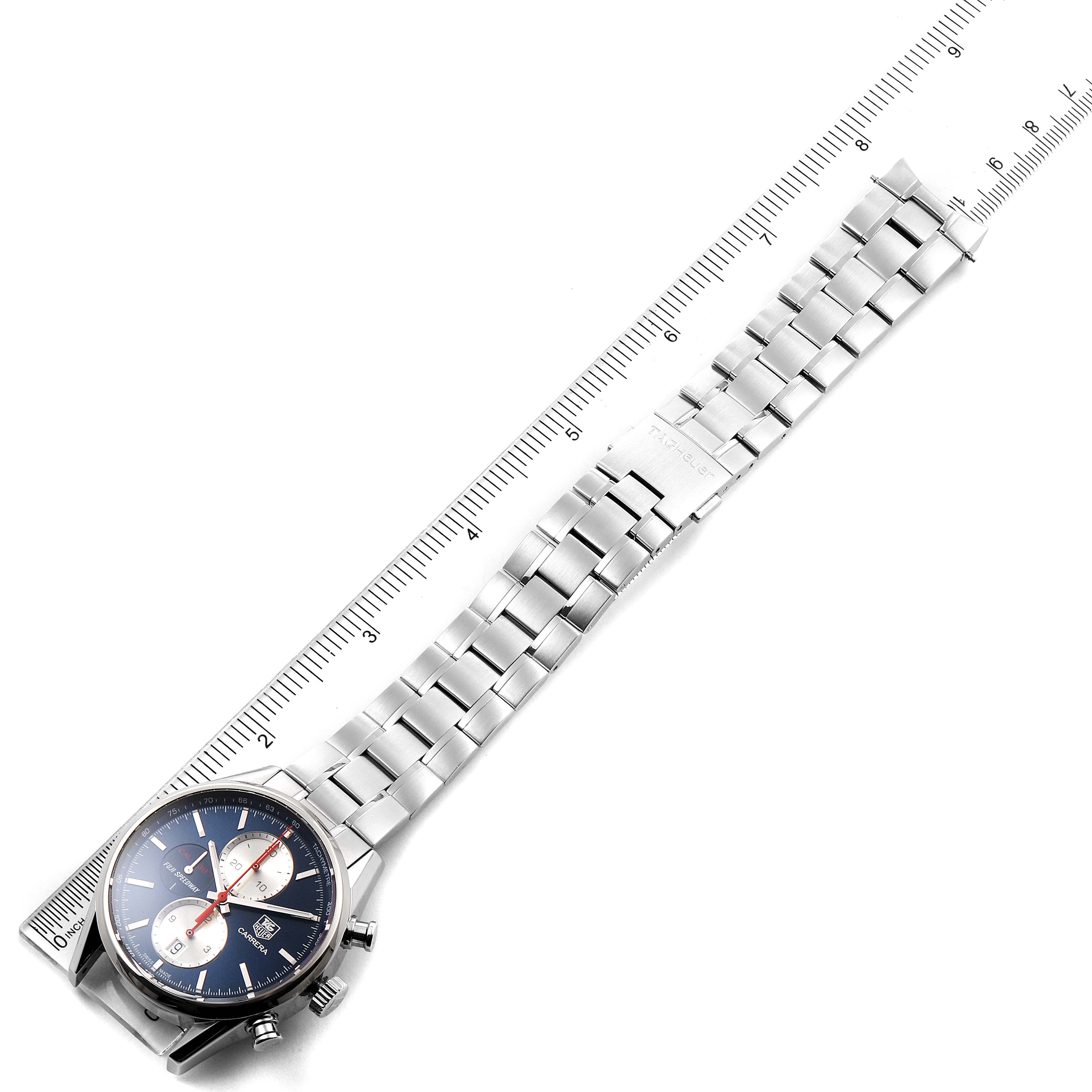This image shows a Tag Heuer Carrera watch laid flat alongside a ruler, displaying the bracelet and dial from an angled top view.