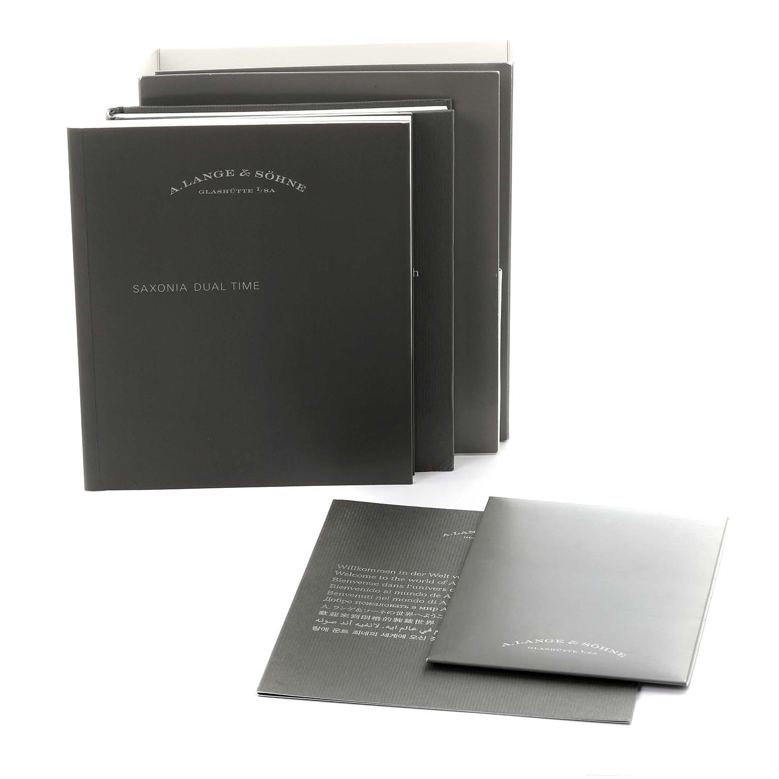 The image shows manuals and booklets for the Saxonia model by A. Lange & Söhne, arranged standing and flat.