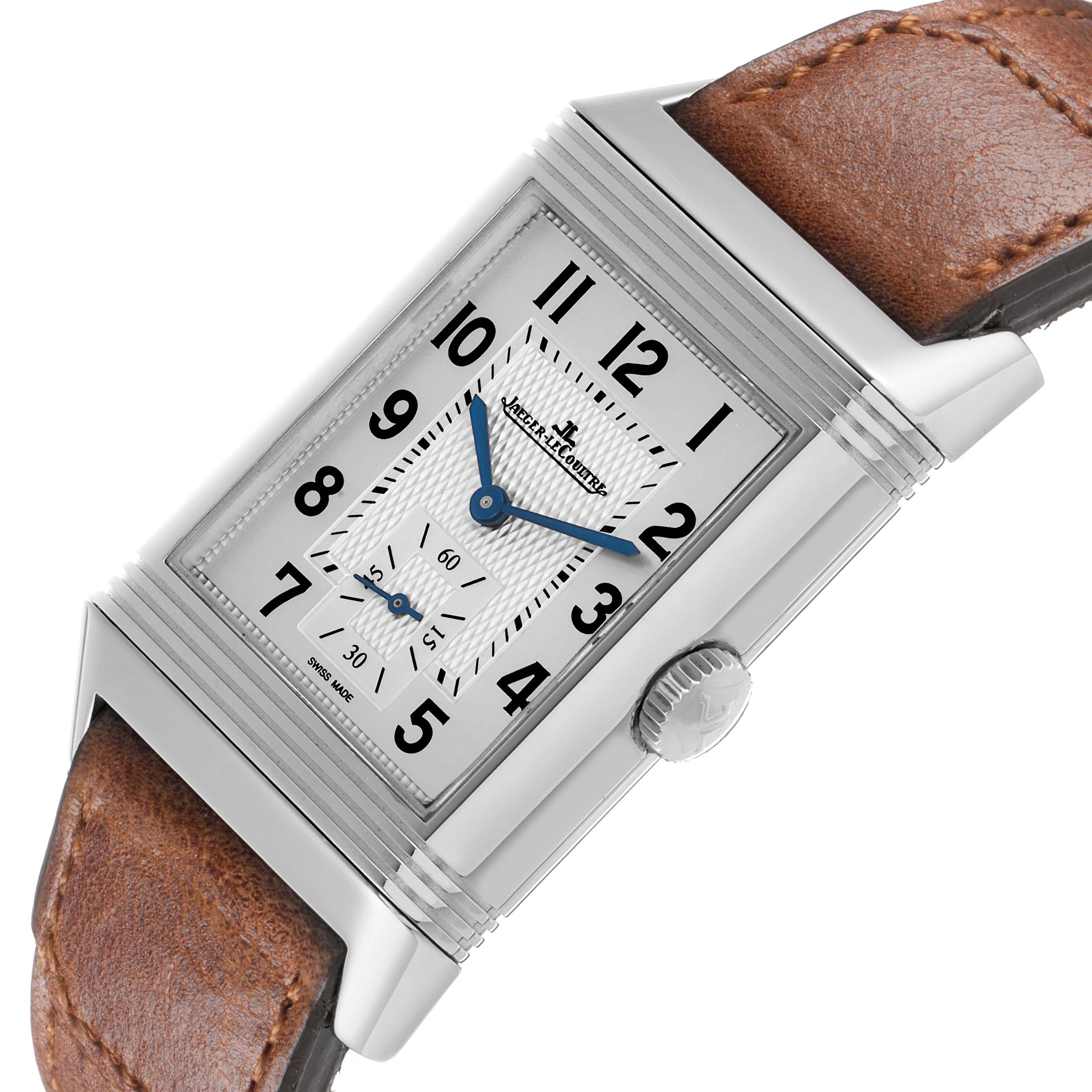 The Jaeger-LeCoultre Reverso watch is shown at an angle displaying its rectangular face, Arabic numerals, blue hands, and brown leather strap.