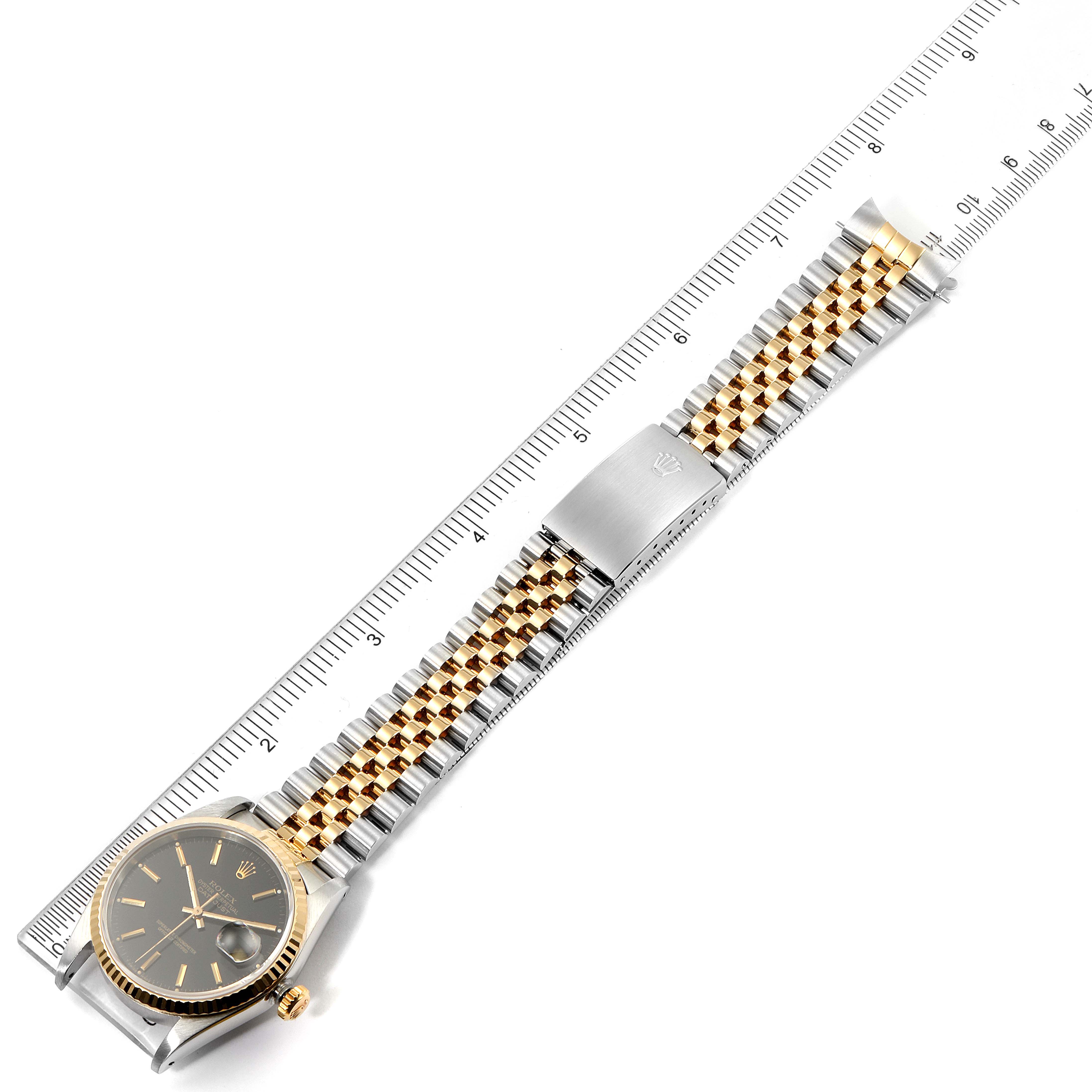 The Rolex Datejust 16233 Men's Steel and Gold (two tone) Black Dial 16233 Men's Steel and Gold (two tone) Black Dial watch is shown from a top-down angle, displaying the face, crown, and Jubilee bracelet next to a ruler.