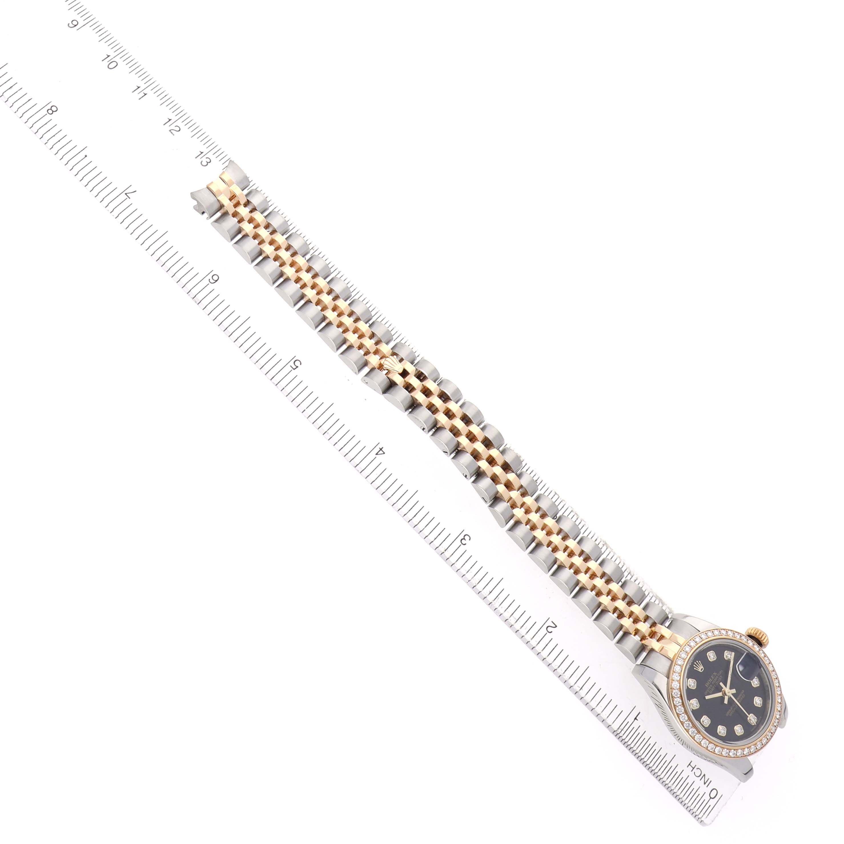 The Rolex Datejust 179383 Women's Steel and Gold (two tone) Black Dial watch is shown from a top-down angle, displaying its bracelet and face next to a ruler for scale.