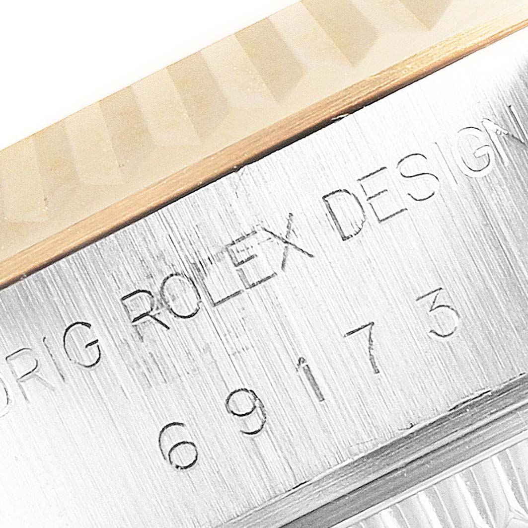 The image shows a close-up angle of a Rolex Datejust 69173 Women
s Steel and Gold (two tone) Silver Dial 69173 Women
s Steel and Gold (two tone) Silver Dial watch with part of its fluted bezel and engraved case serial number visible.