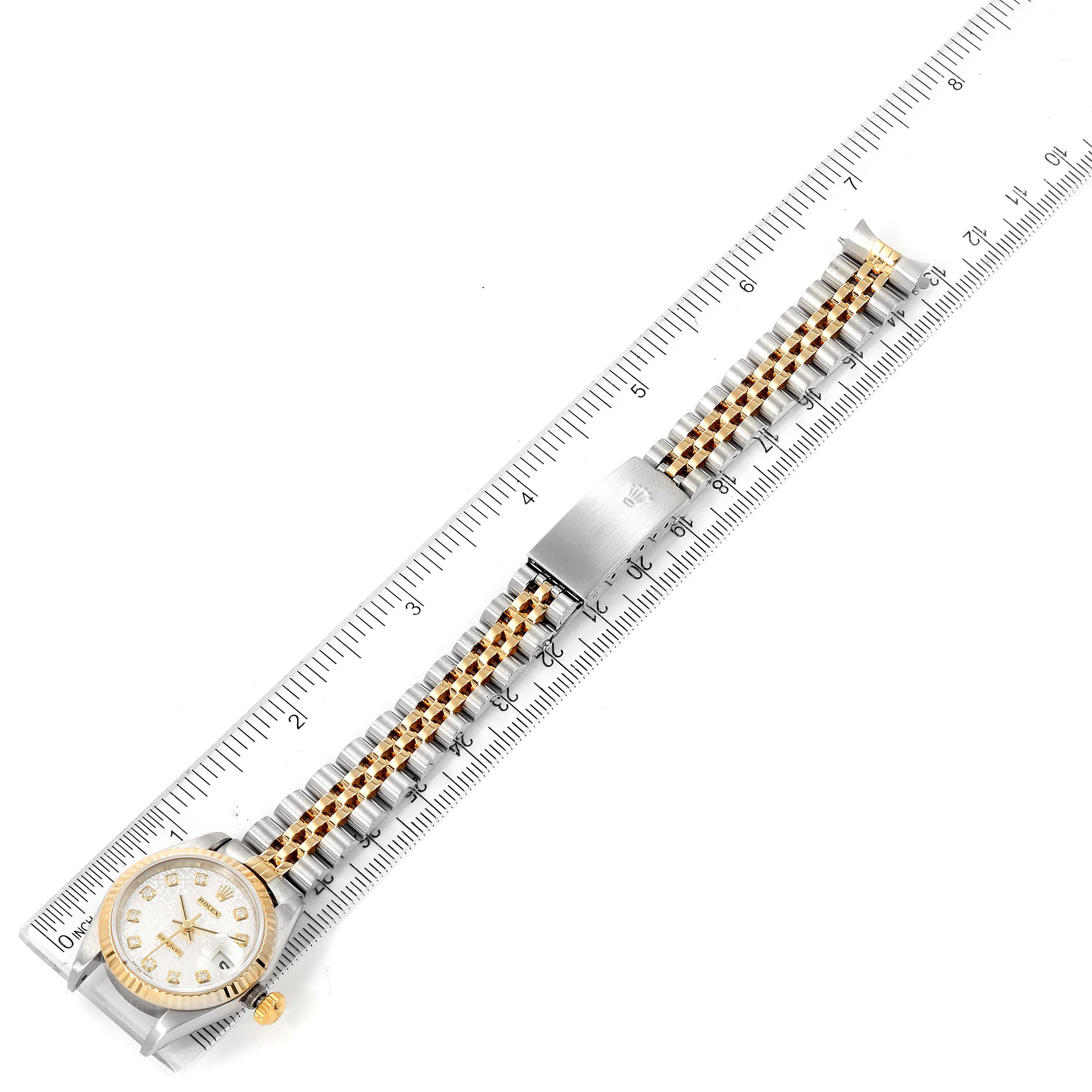 The image shows a top-view angle of a Rolex Datejust 79173 Women
s Steel and Gold (two tone) Silver Dial 79173 Women
s Steel and Gold (two tone) Silver Dial watch, featuring its dial, case, and two-tone bracelet laid on a ruler.