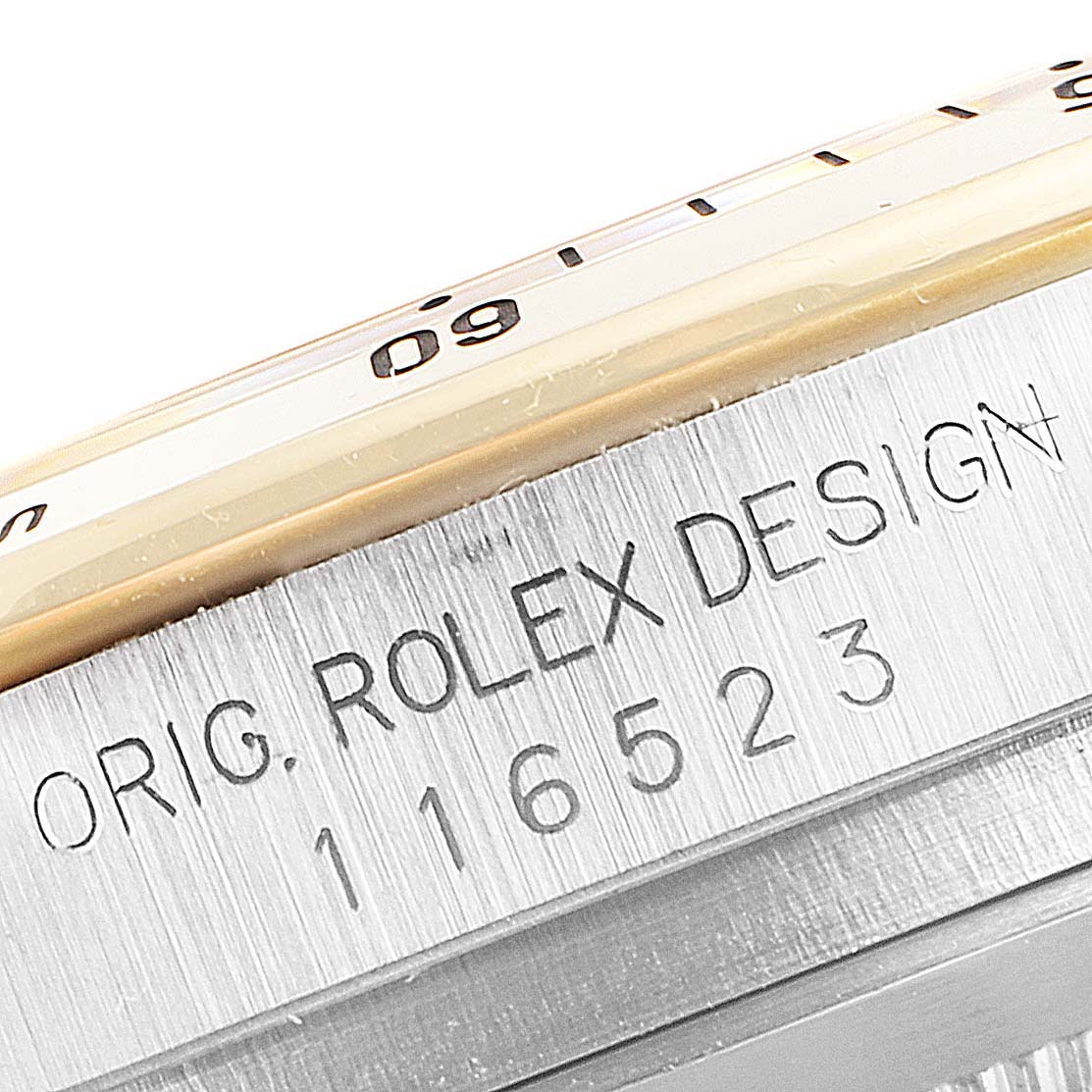 This image shows a close-up view of the case and bezel of a Rolex Daytona 116523 Men's Steel and Gold (two tone) Grey Dial 116523 Men's Steel and Gold (two tone) Grey Dial, displaying the serial number and "Rolex Design" engraving.