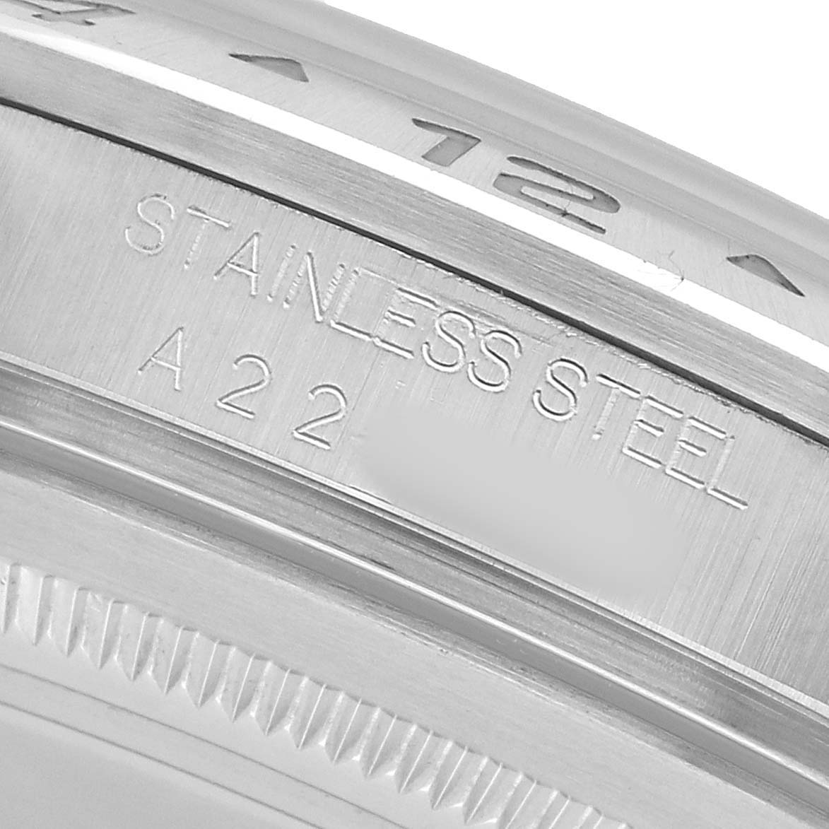 The image shows a close-up of the bezel and engraving on a Rolex Explorer 16570 Men's Stainless Steel White Dial, highlighting "STAINLESS STEEL" and a partial serial/production code.