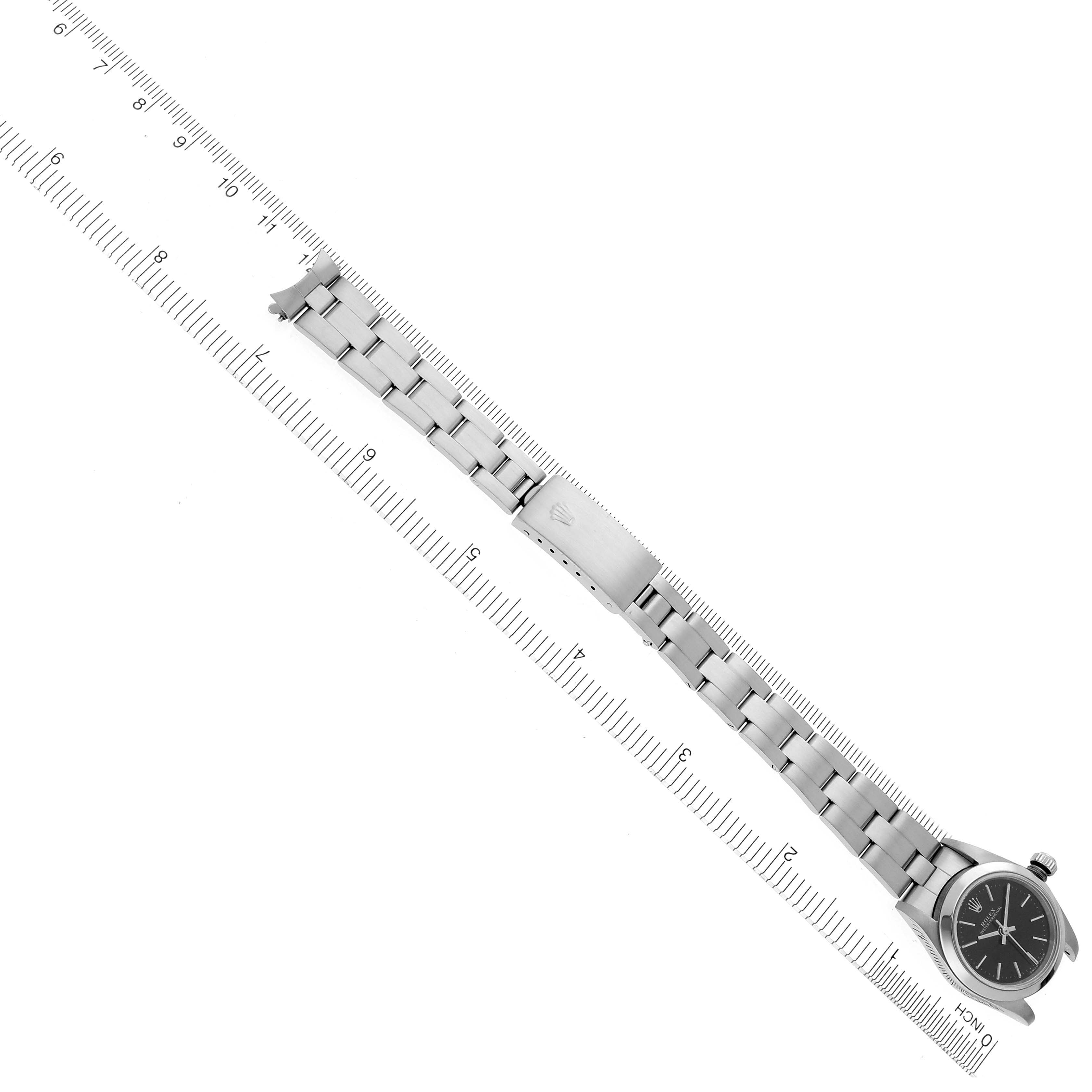 The Rolex Oyster Perpetual 76080 Women's Stainless Steel Black Dial 76080 Women's Stainless Steel Black Dial watch is shown diagonally with its bracelet fully extended alongside a ruler.