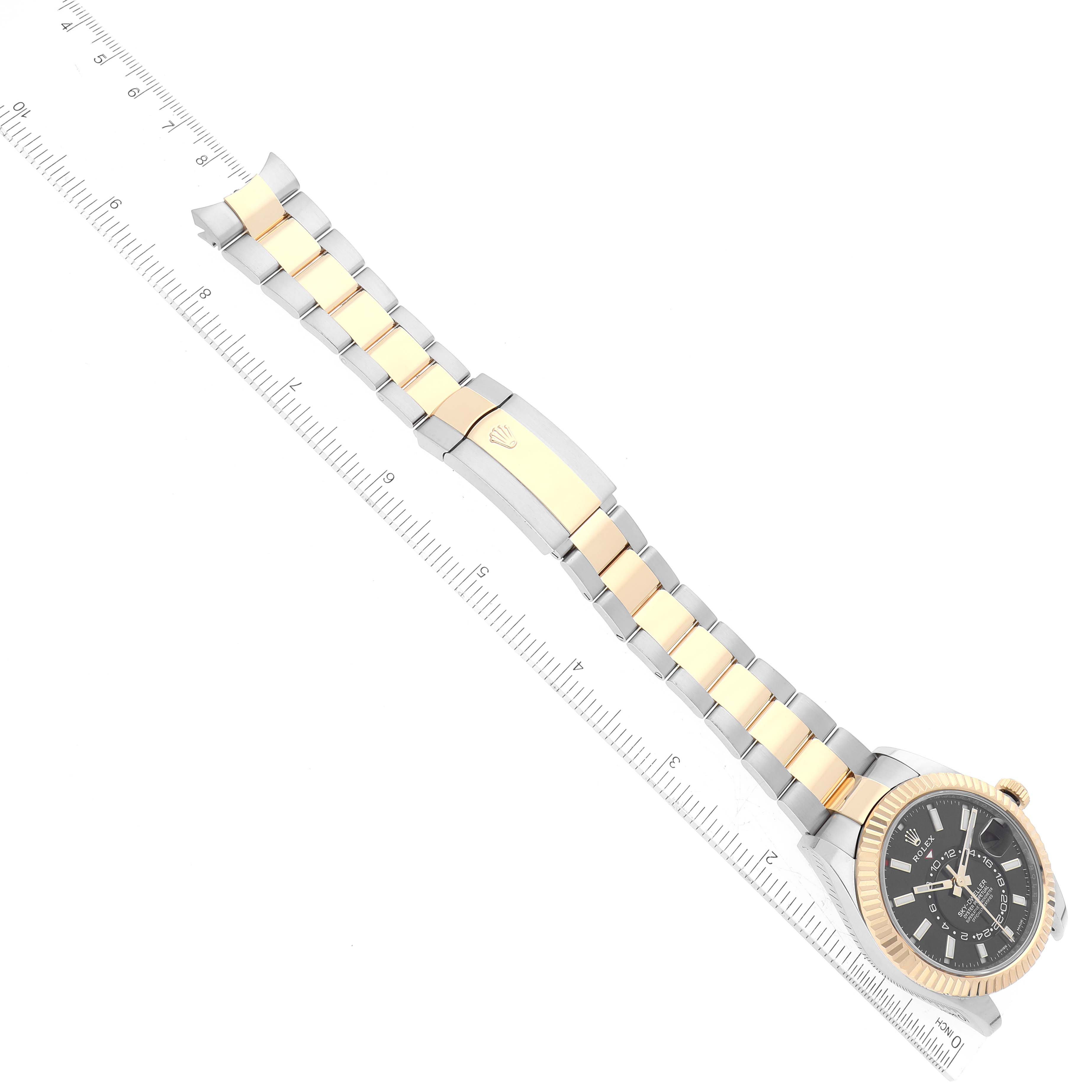 The image shows the full length of a Rolex Sky-Dweller 326933 Men
s Steel and Gold (two tone) Black Dial 326933 Men
s Steel and Gold (two tone) Black Dial watch, including its bracelet with a two-tone design, laid flat next to a ruler.