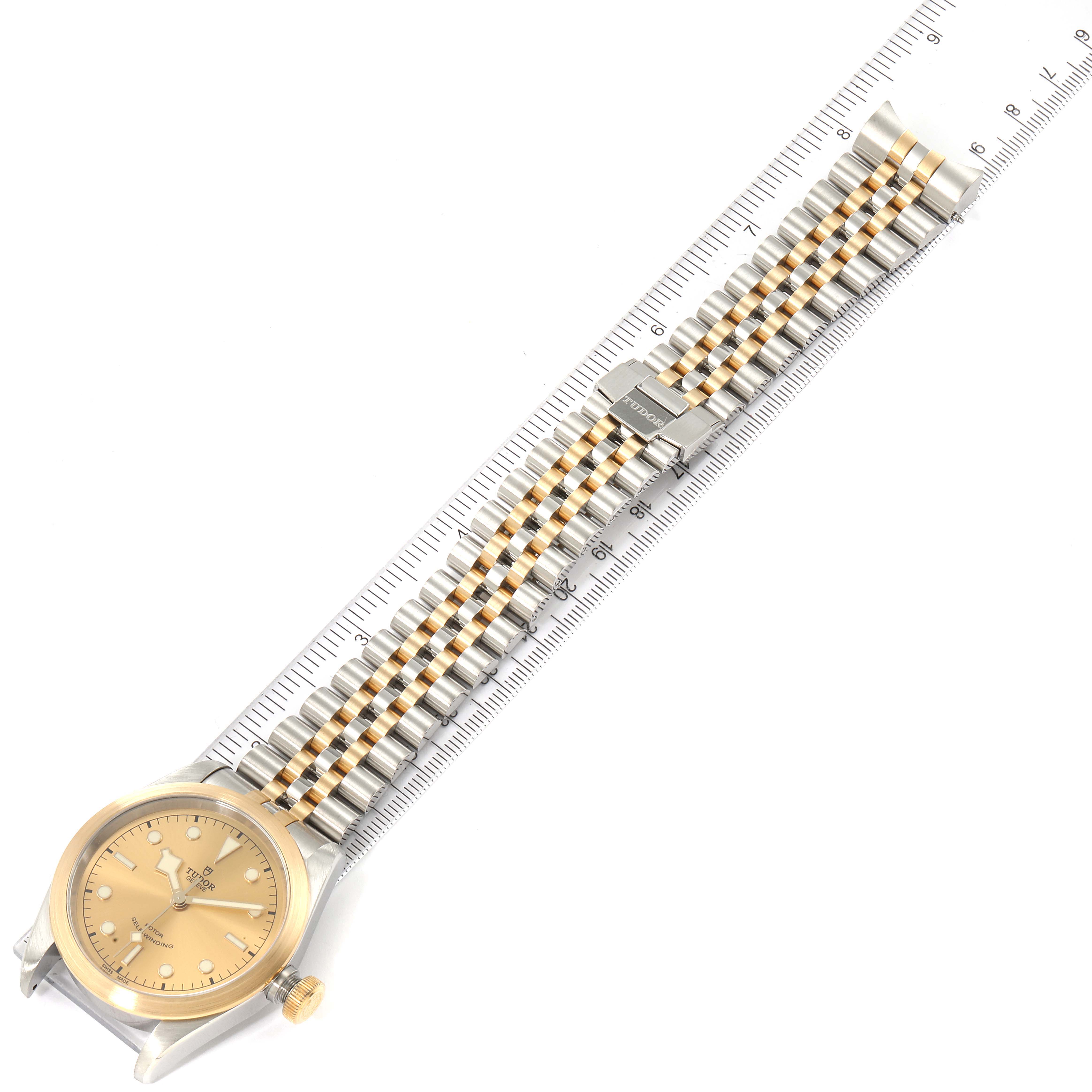 The image shows a Tudor Heritage Black Bay 79543 Men's Steel and Gold (two tone) Champagne Dial 79543 Men's Steel and Gold (two tone) Champagne Dial watch with a ruler for scale, displaying its gold and silver bracelet and face from a top view.