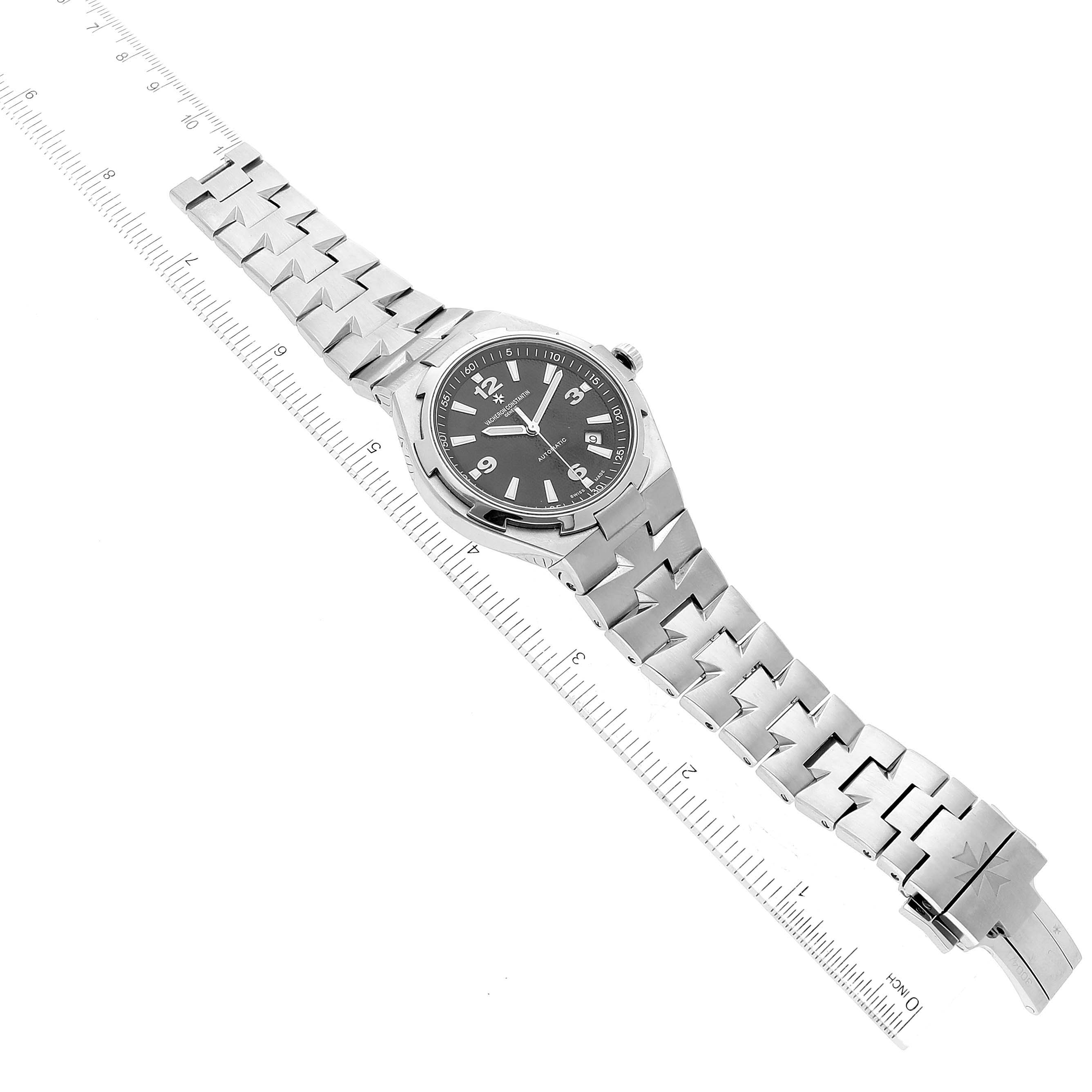 The Vacheron Constantin Overseas 47040/B01A-9094 Men's Stainless Steel Black Dial 47040/B01A-9094 Men's Stainless Steel Black Dial watch is shown at an oblique angle, displaying the face, bracelet, and clasp with a ruler for scale.