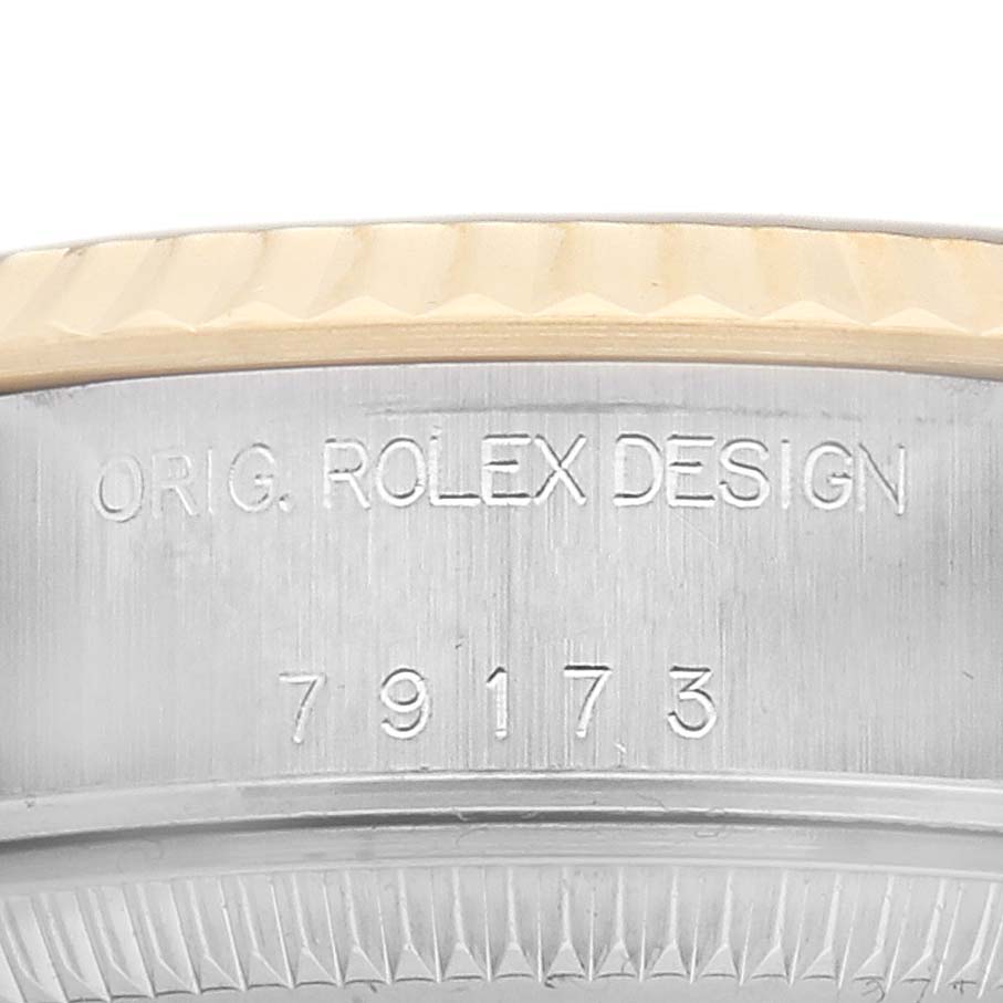 The image shows a close-up of the Rolex Datejust 79173 Women's Steel and Gold (two tone) Champagne Dial model's case with engraved text and a fluted bezel.
