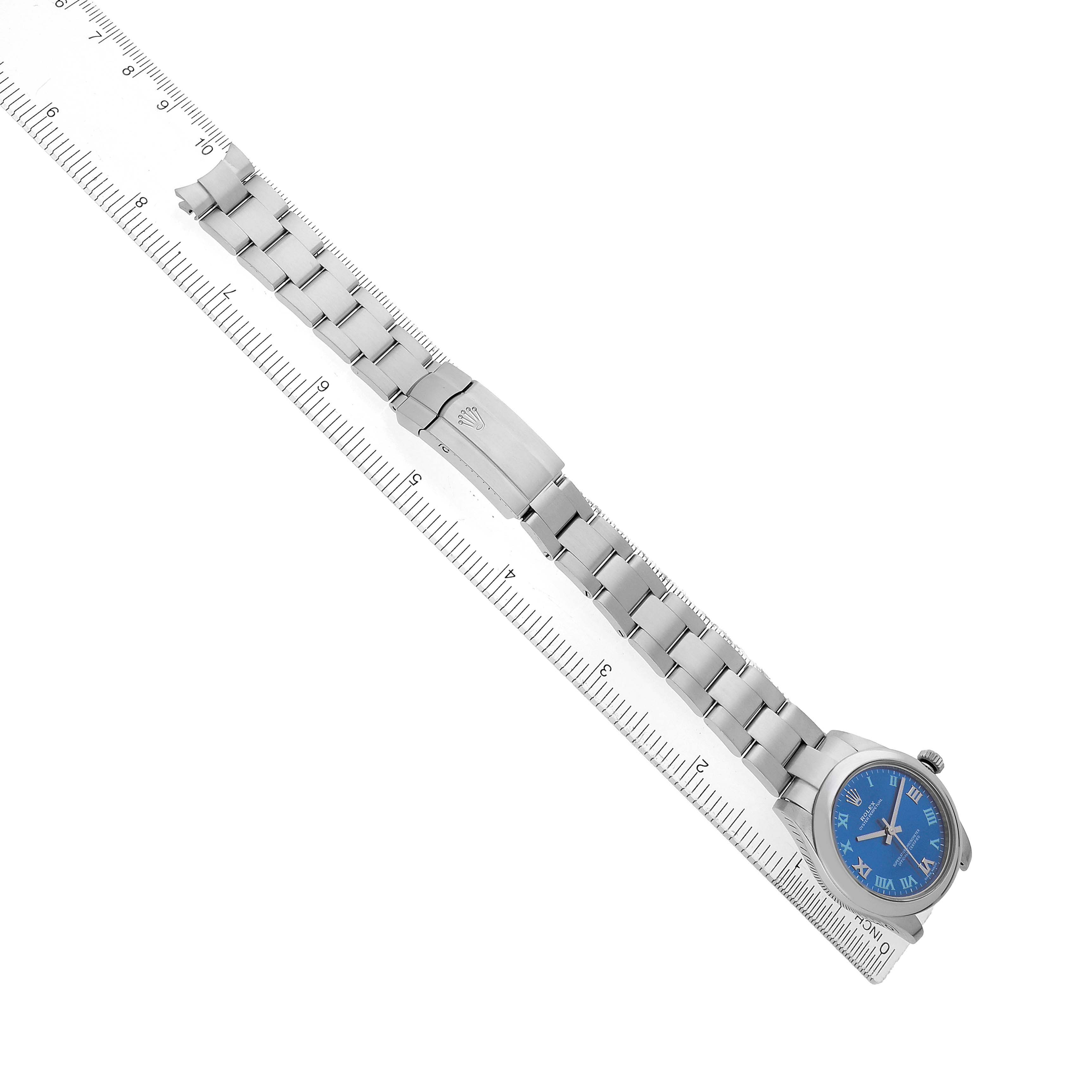 The Rolex Mid-Size 177200 Women's Stainless Steel Blue Dial watch is displayed diagonally with the full bracelet, clasp, and blue dial visible, aligned next to a ruler.