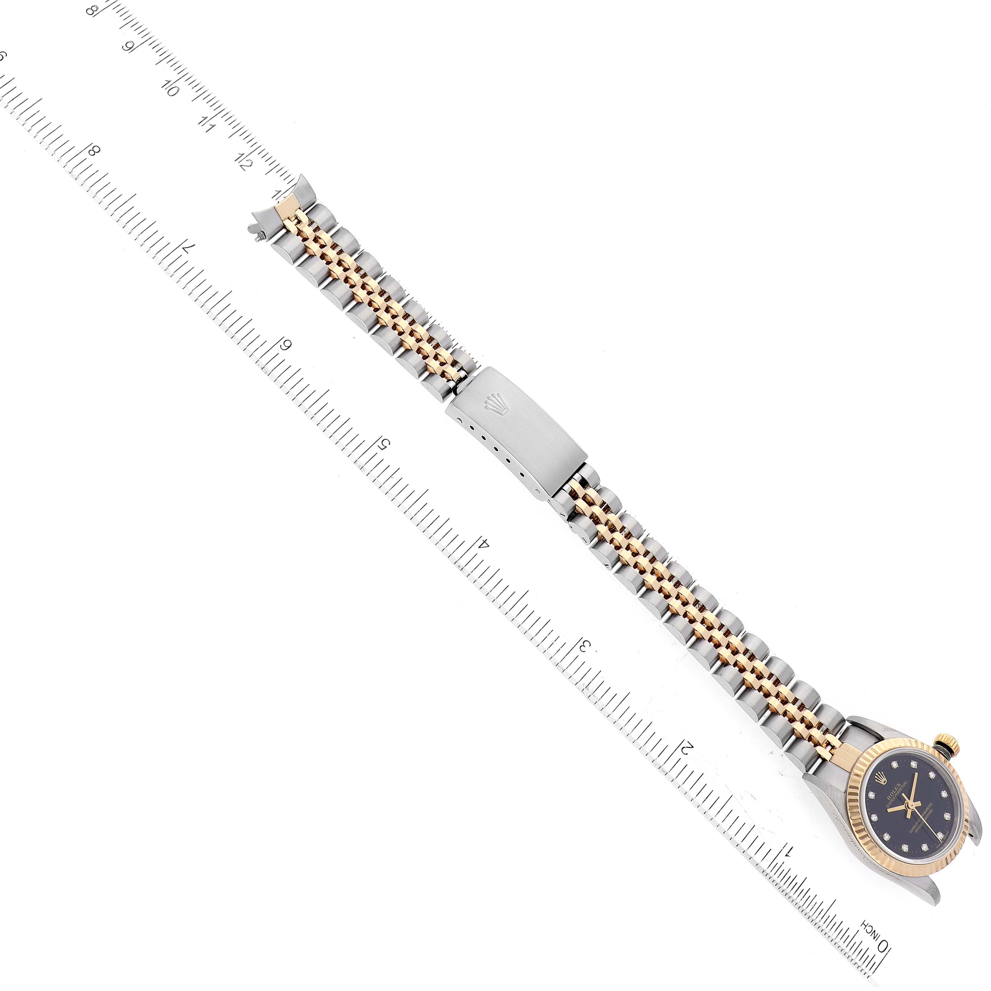 The image shows a top view of a Rolex Oyster Perpetual 76193 Women's Steel and Gold (two tone) Black Dial 76193 Women's Steel and Gold (two tone) Black Dial watch including its full bracelet and clasp, with a ruler for scale.