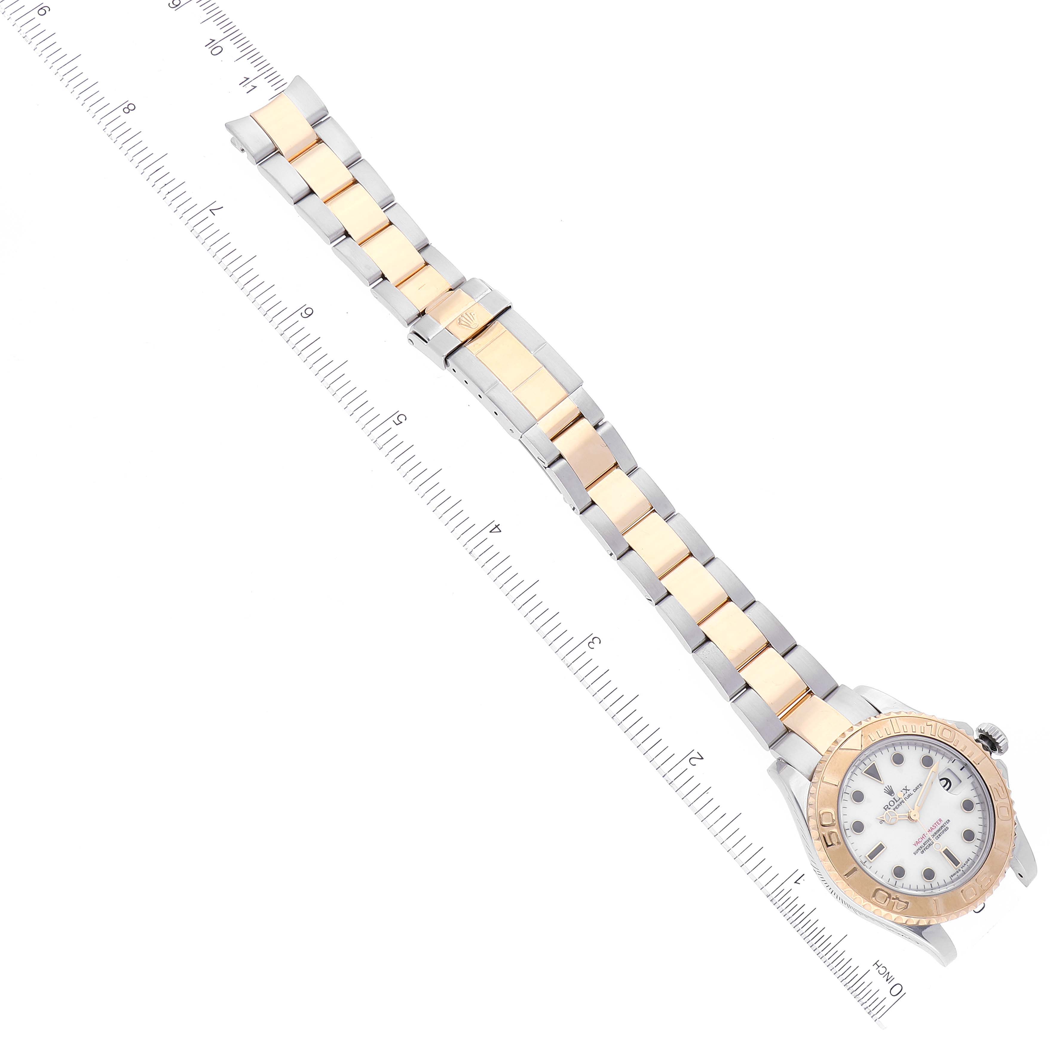 The image shows a Rolex Yacht-Master 168623 Women's Steel and Gold (two tone) White Dial 168623 Women's Steel and Gold (two tone) White Dial watch with a focus on its full band laying alongside a ruler.