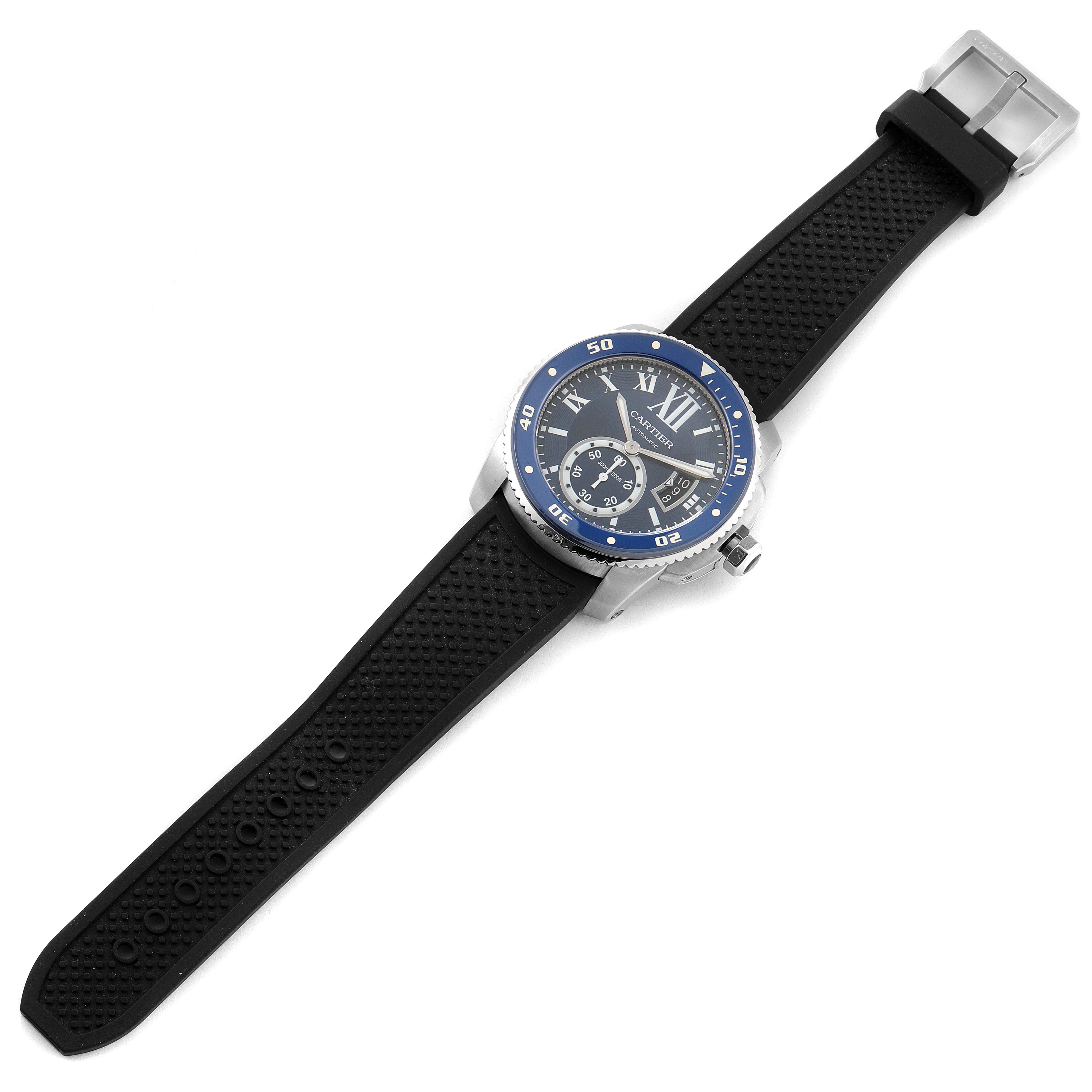The image shows a Calibre de Cartier watch with a black rubber strap, blue bezel, and silver-tone case from an overhead angle.
