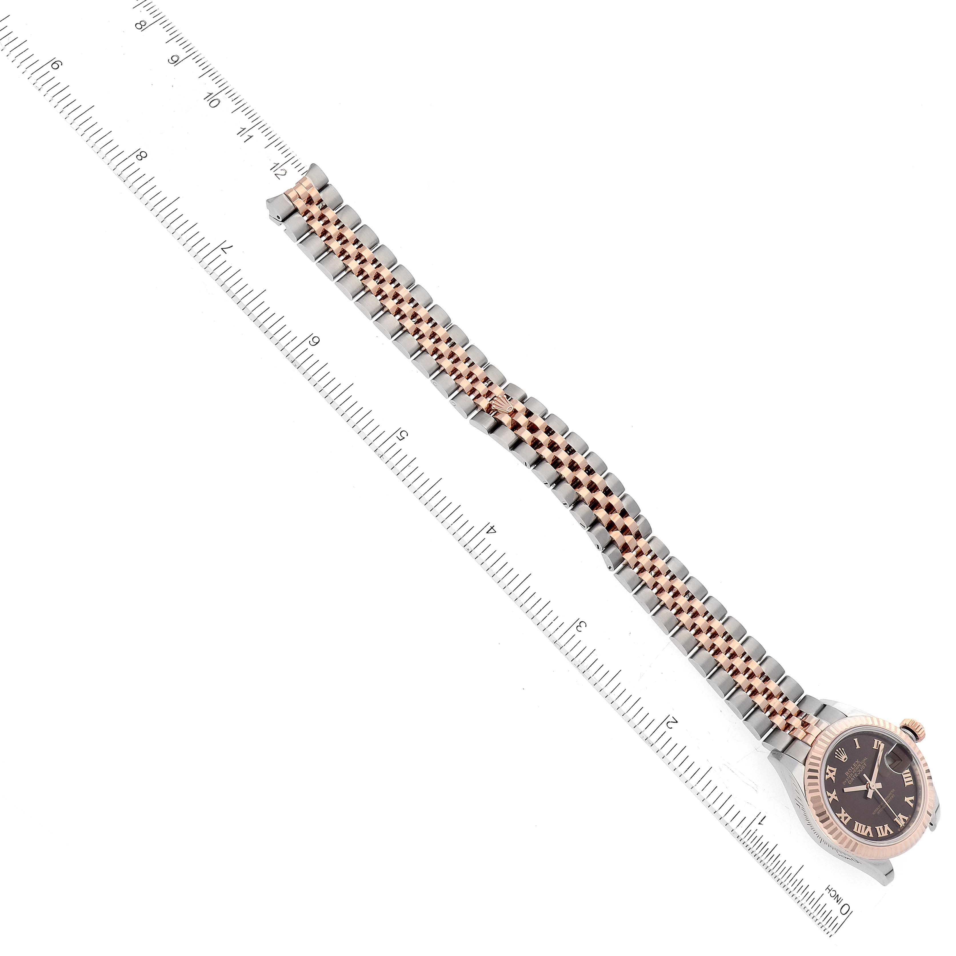 This image shows a top view of a Rolex Datejust 279171 Women's Steel and Gold (two tone) Brown Dial 279171 Women's Steel and Gold (two tone) Brown Dial watch with its face and metal band placed alongside a ruler.
