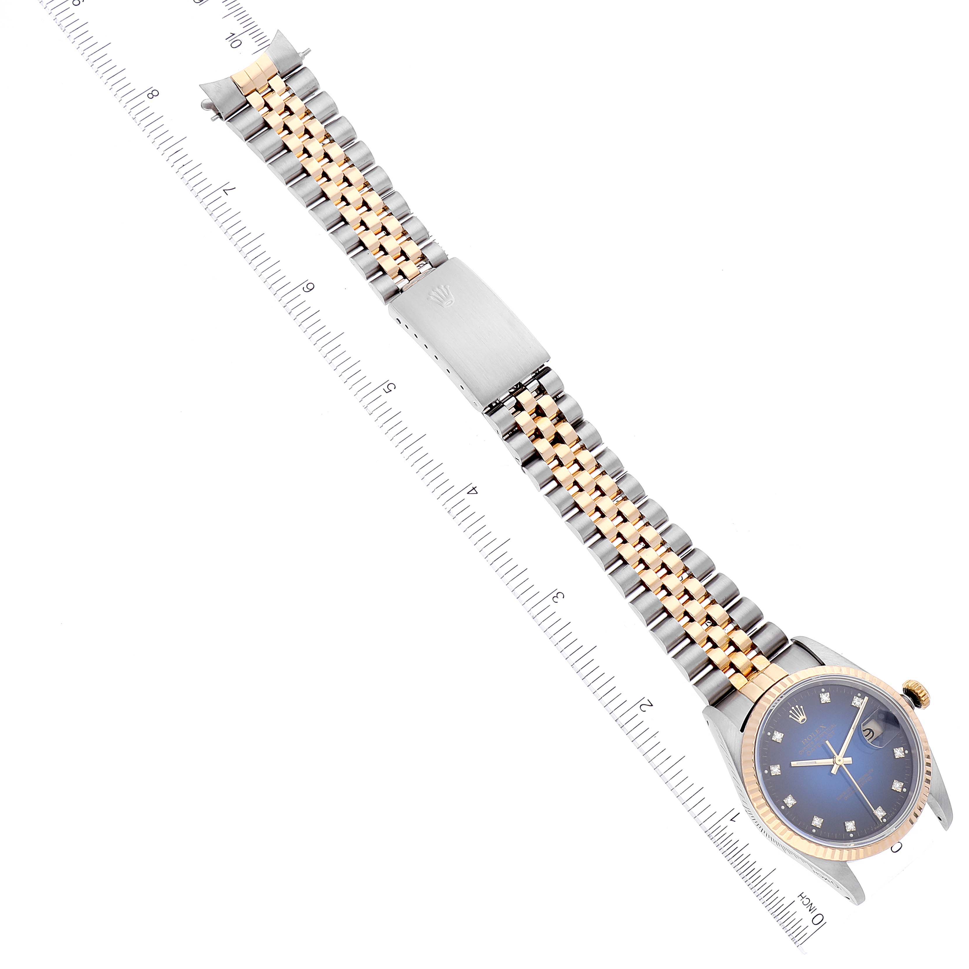 The image shows a full view at a diagonal angle of the Rolex Datejust 16233 Men's Steel and Gold (two tone) Blue Dial 16233 Men's Steel and Gold (two tone) Blue Dial watch, displaying its face and jubilee bracelet beside a ruler.
